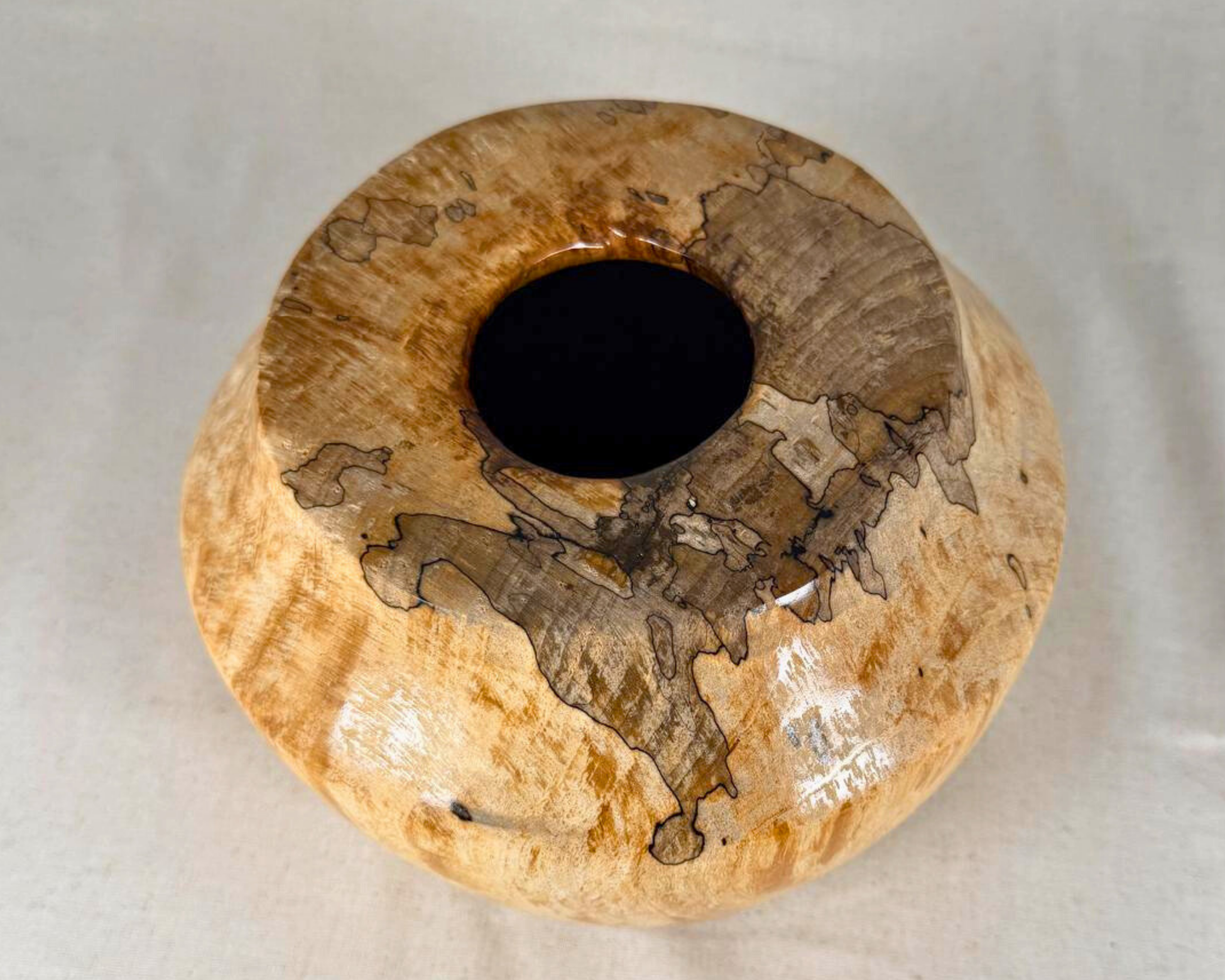 Top view of a spalted maple vessel, showing the circular opening surrounded by pale maple and an asymmetrical field of dark spalting spreading across the top.