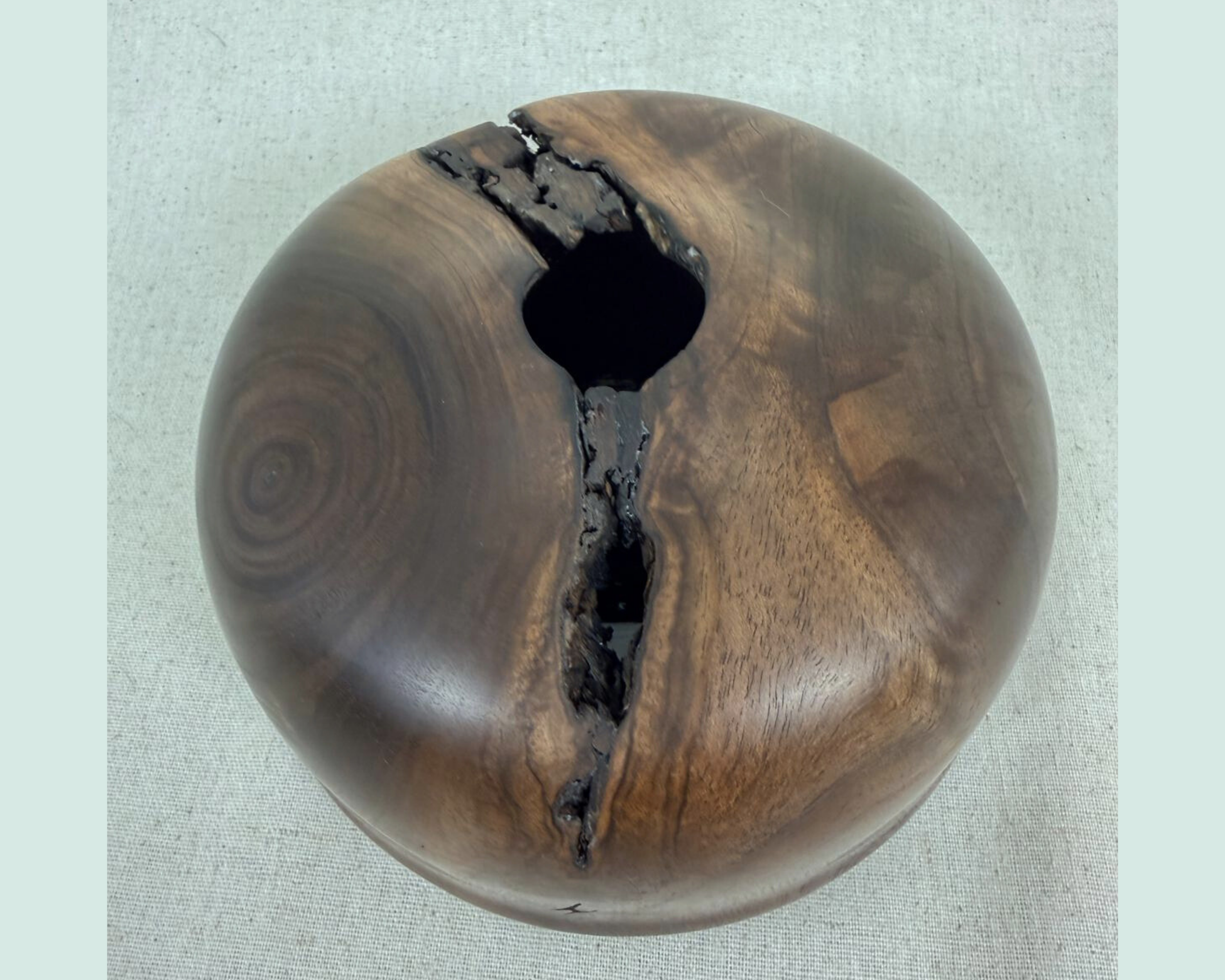 Top view of a walnut vessel with a small central opening and a long natural fissure that reveals voids extending fully through the piece.