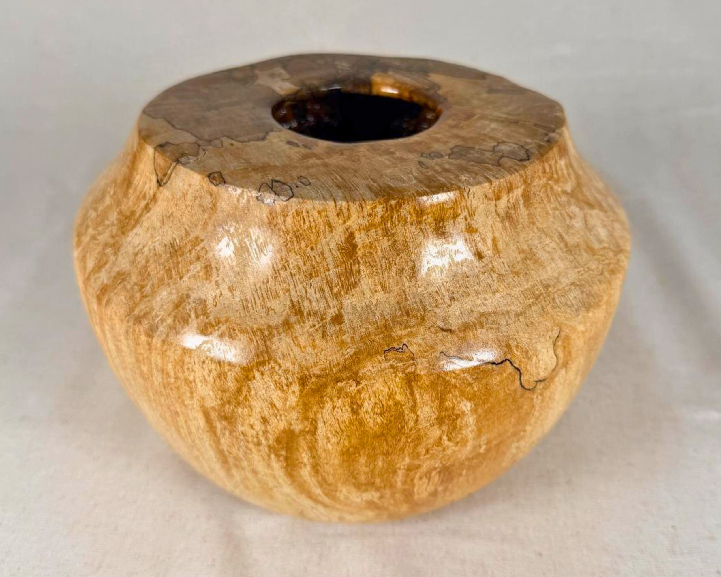 Spalted maple vessel viewed from the front, emphasizing the low rounded body, tapered shoulder, and irregular dark spalting around the rim.