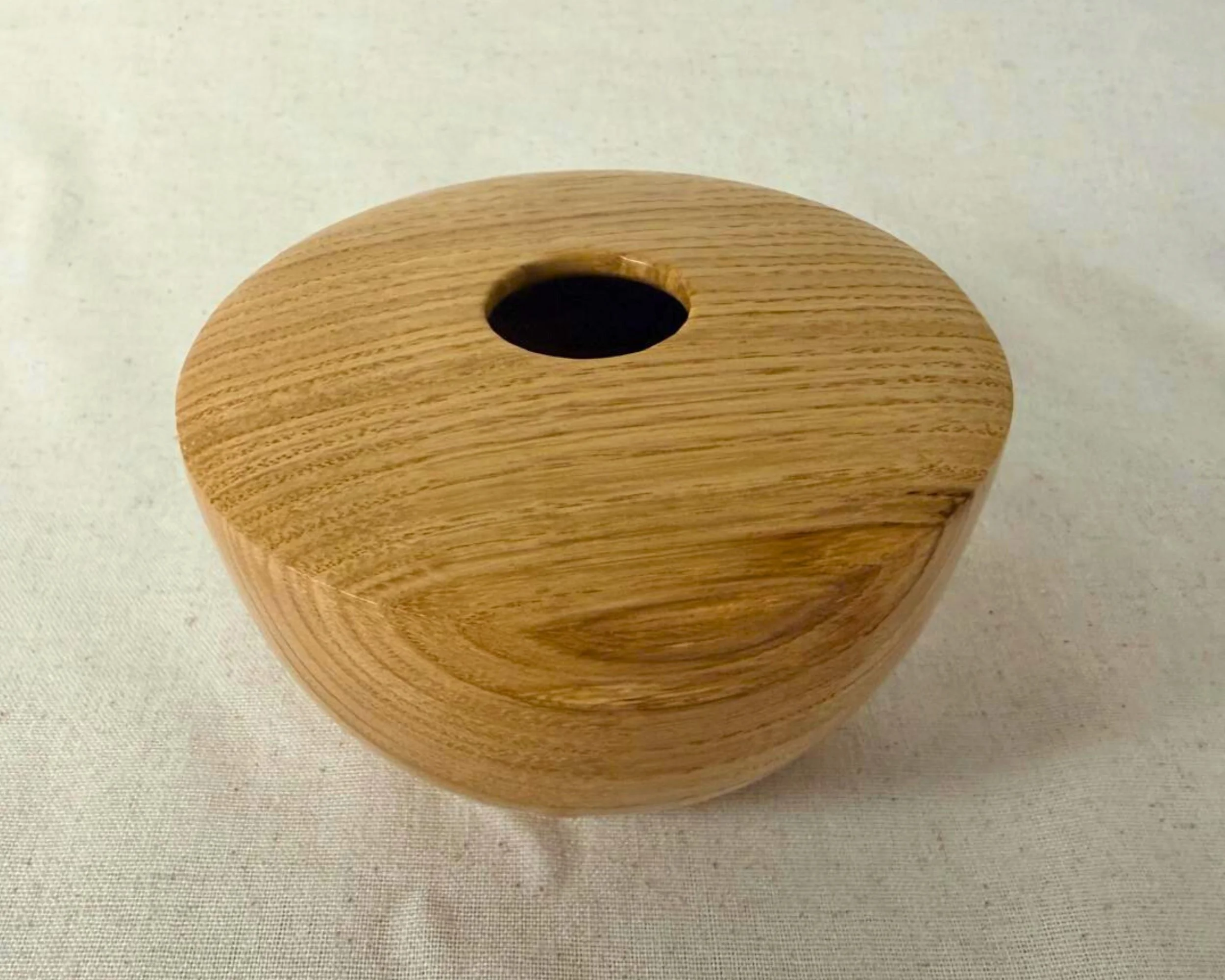 Angled view of the oak hollow form showing the top plane, opening, and curved shoulder.
