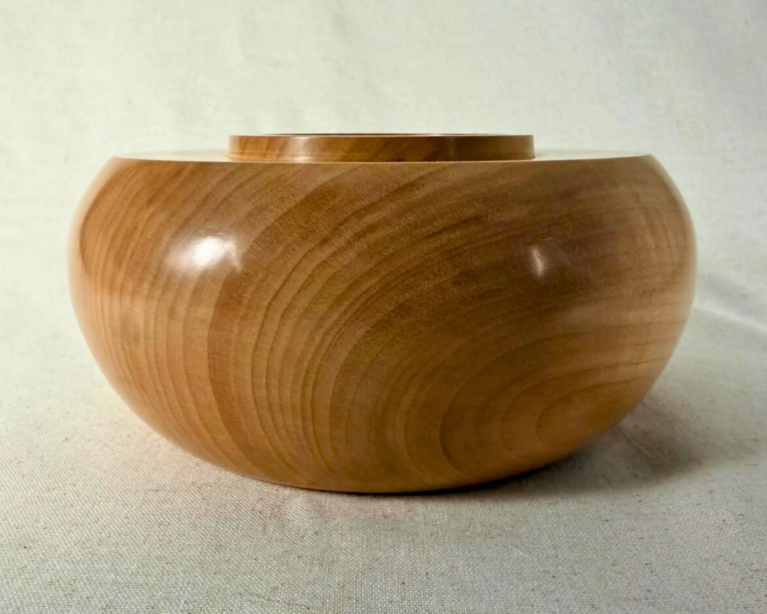 Side profile view of a maple closed form vessel showing the low wide silhouette and raised collar opening.