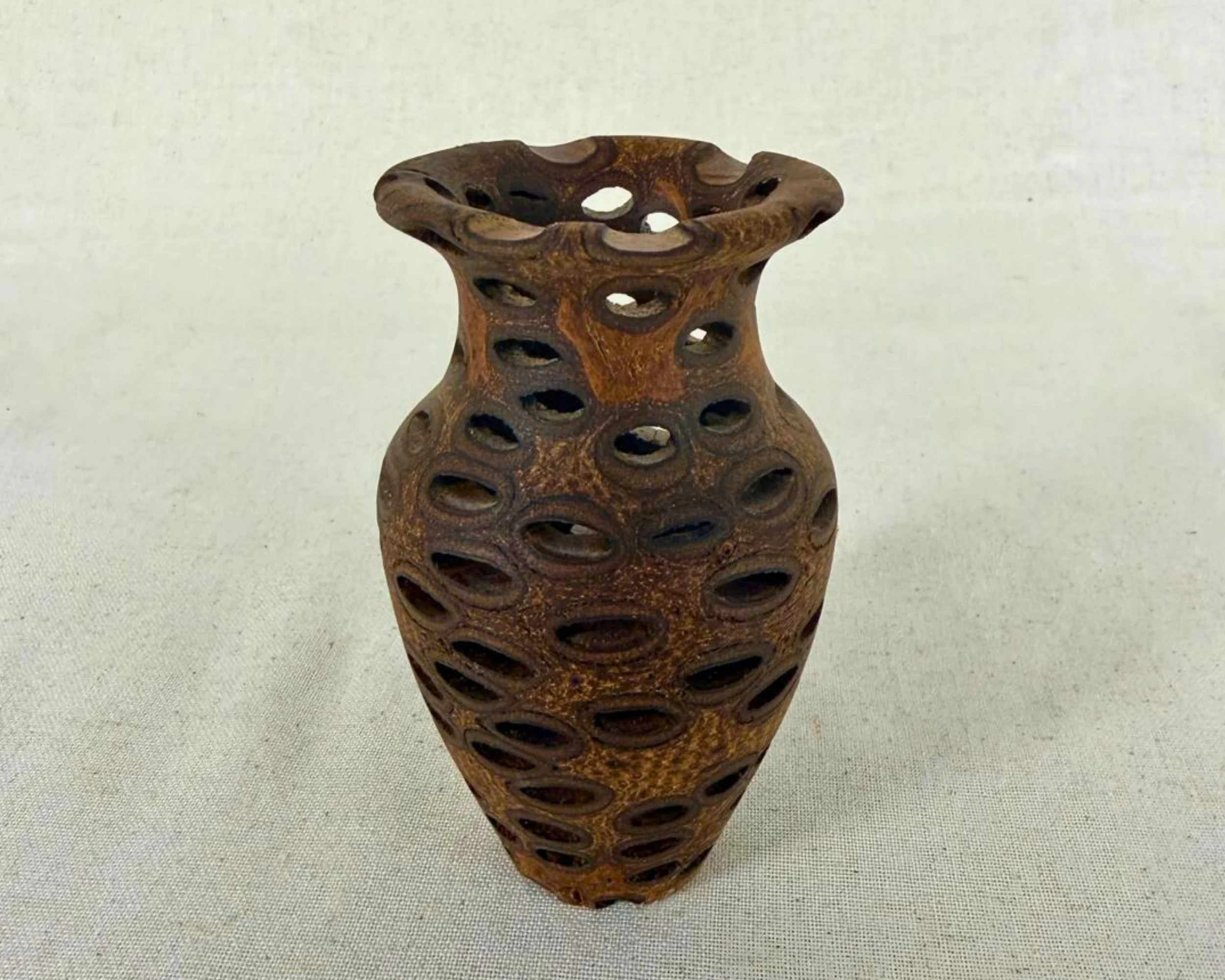 Banksia nut vase with pierced oval openings and flared rim, front view on neutral background.