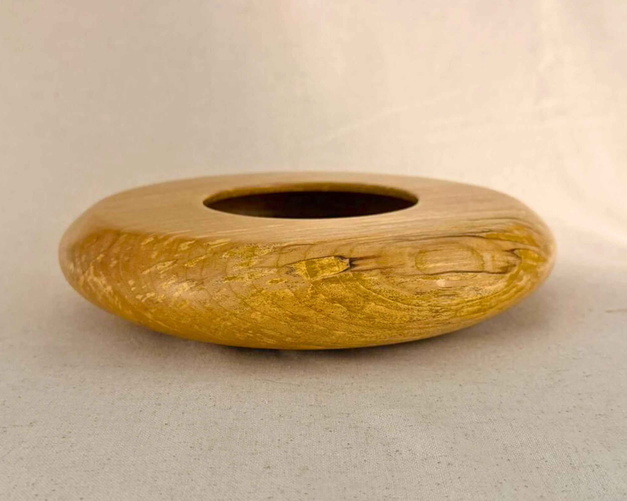 Side profile of a figured maple closed form vessel showing the low height and rounded, flattened form.
