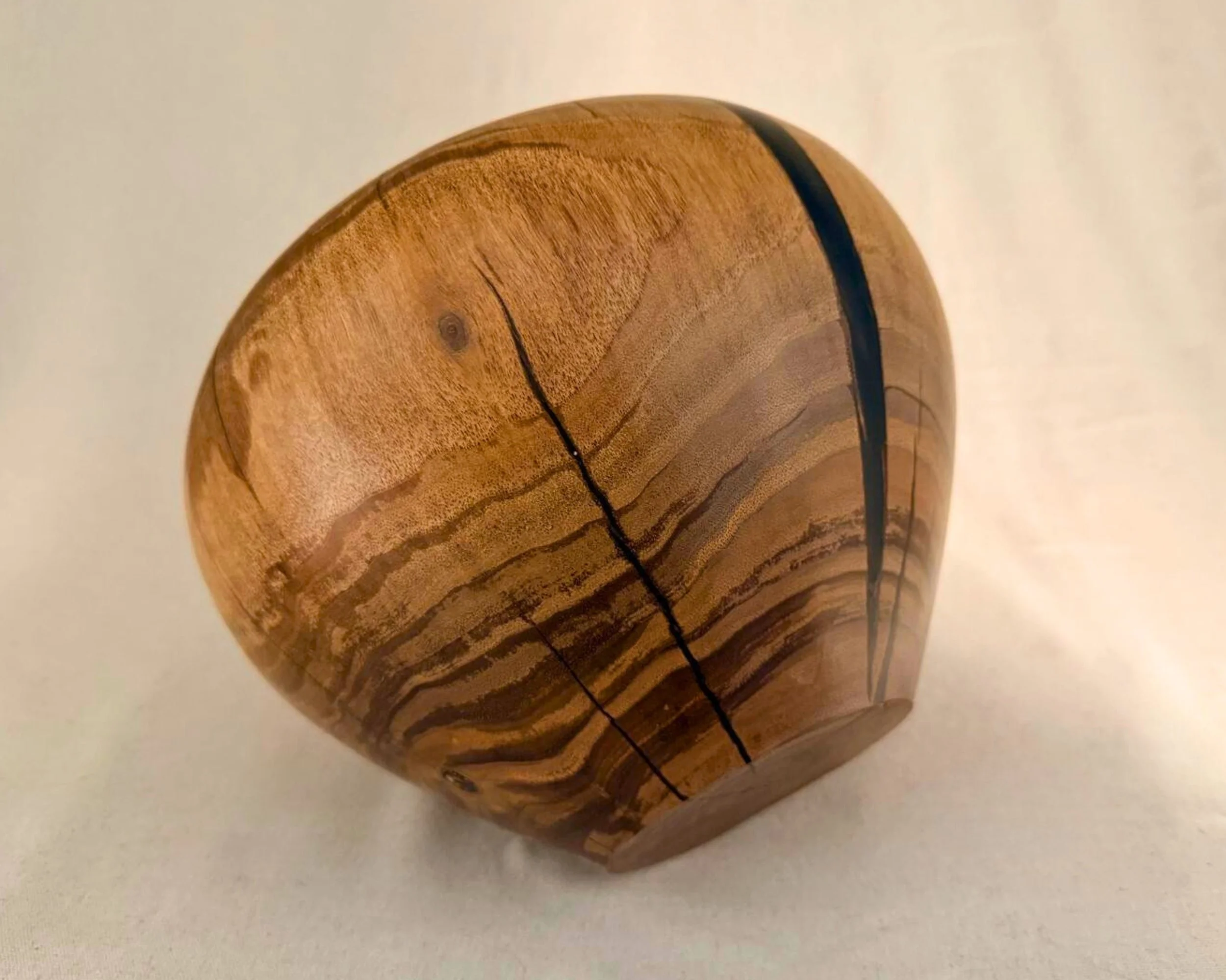 Walnut vessel photographed on its side showing base profile, strong grain striping, and dark epoxy vein line.