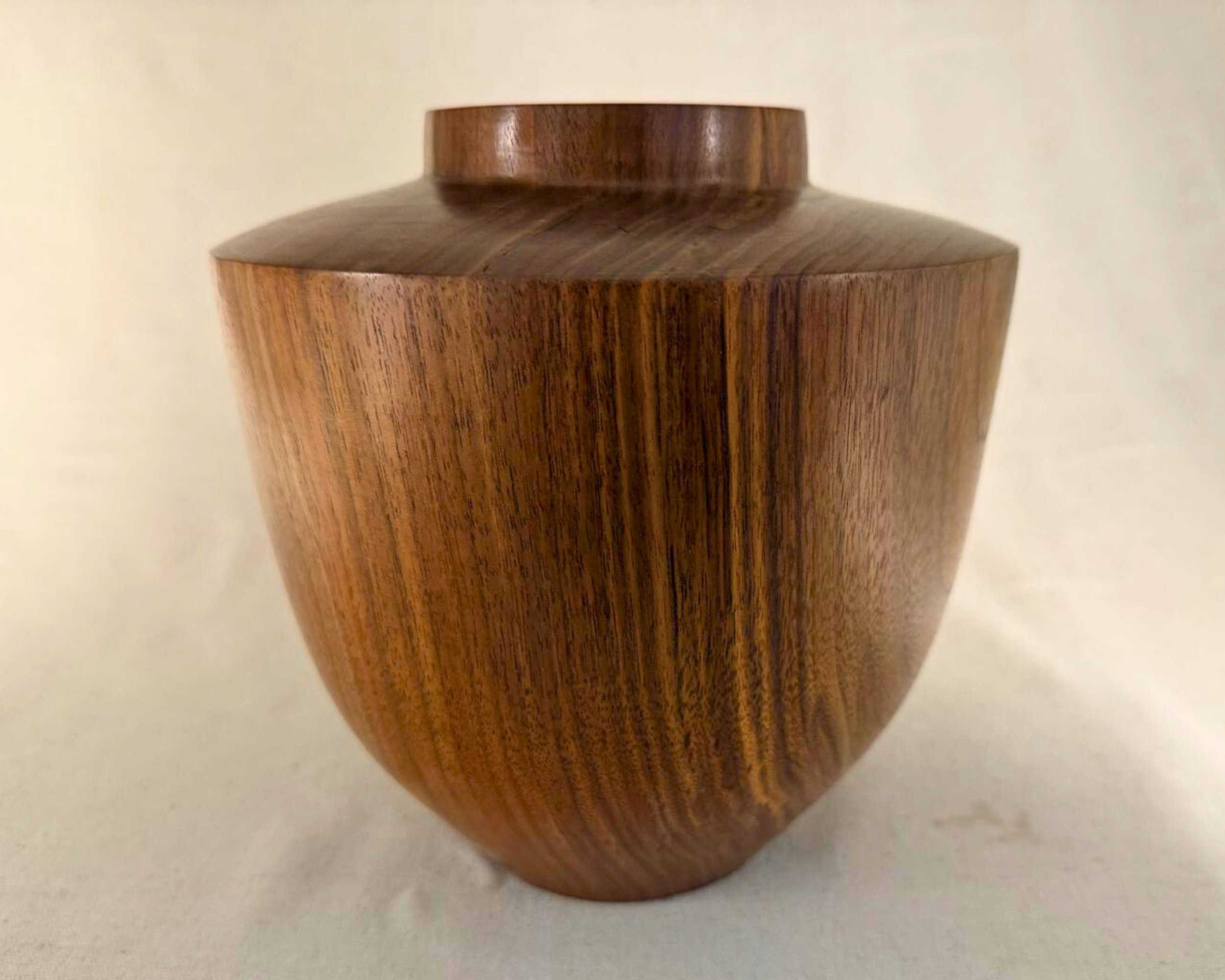 Side profile of walnut vessel with rounded body, wide shoulder, and raised collar opening; dramatic walnut grain visible.