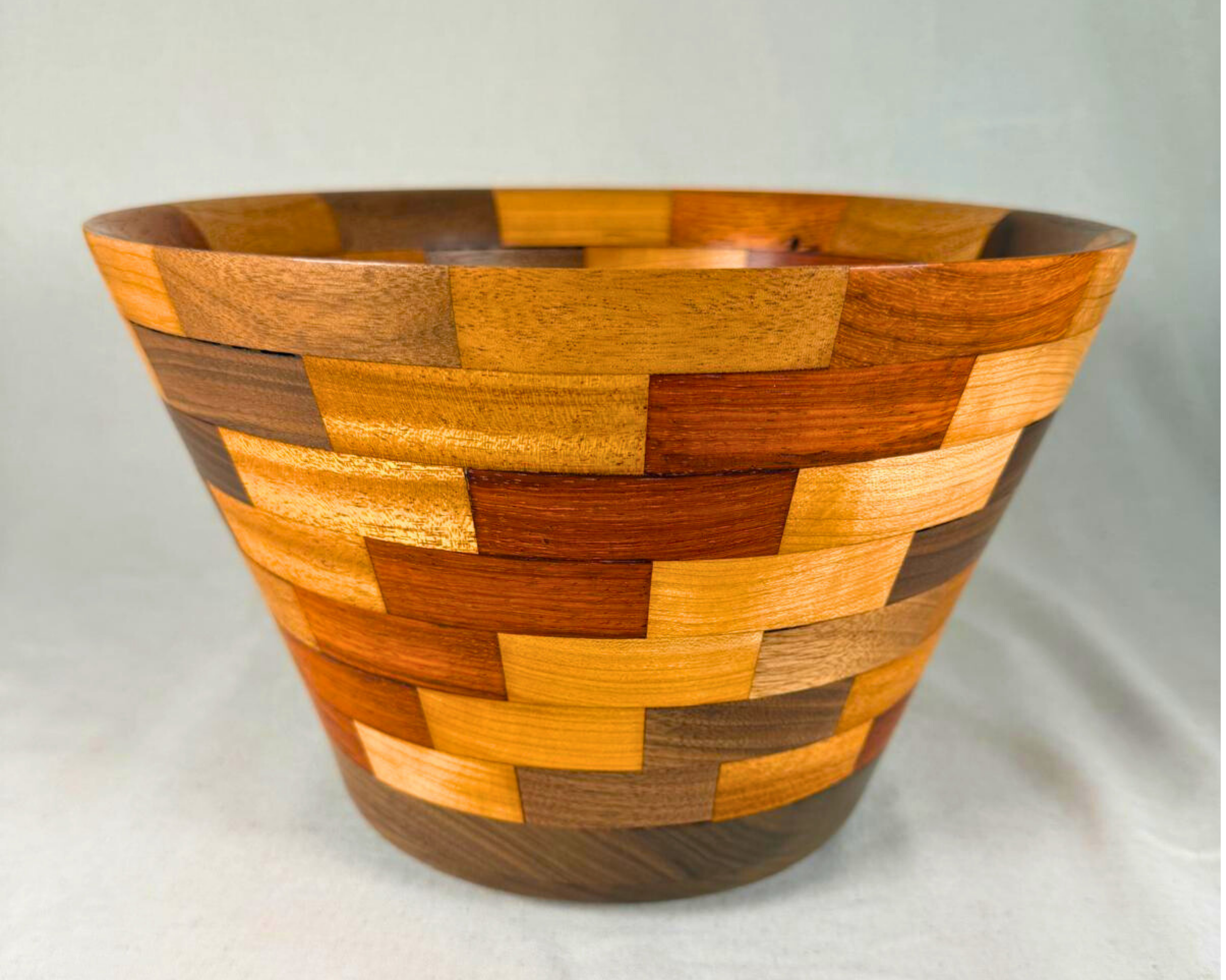 Three-quarter view of the segmented wood vessel showing the broad open rim, flared silhouette, and alternating blocks of contrasting hardwoods.