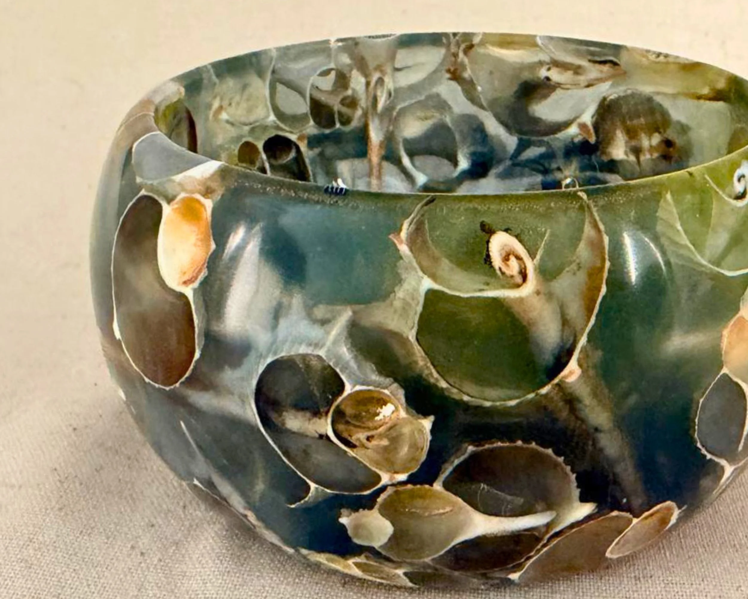 Close-up of green-blue epoxy vessel rim showing embedded real seashell fragments beneath glossy resin.