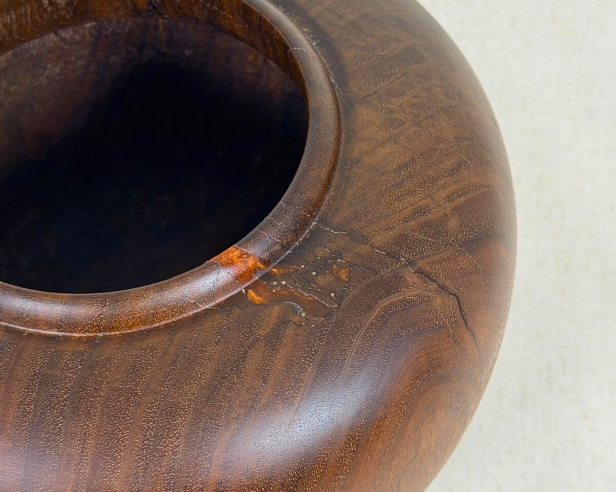 Close-up of a hand-turned dark wood vessel showing the rounded rim, fine grain, and a small amber-toned natural inclusion near the opening.