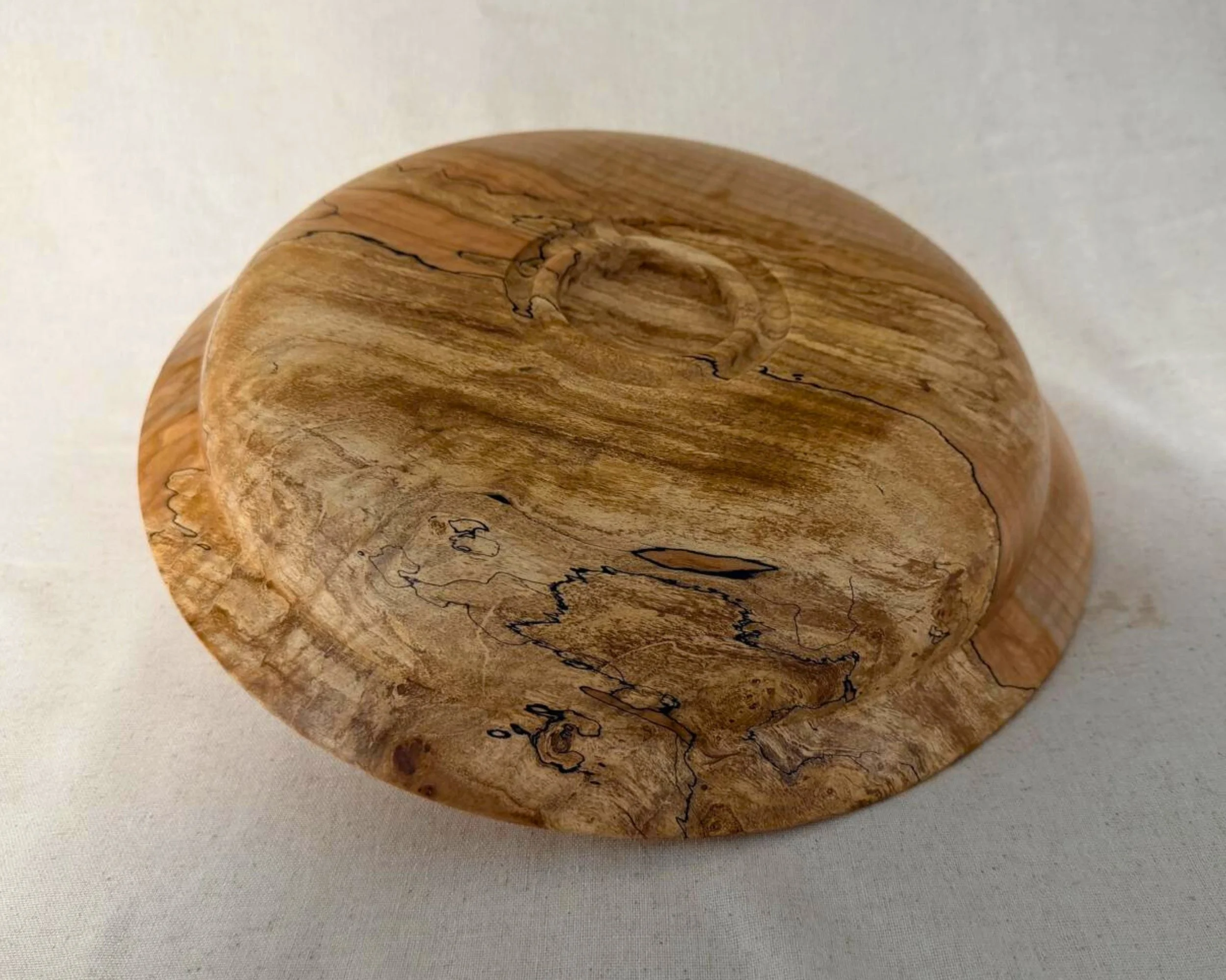 Bottom view of a hand-turned wooden platter showing the recessed foot ring, figured grain, and natural spalted character.