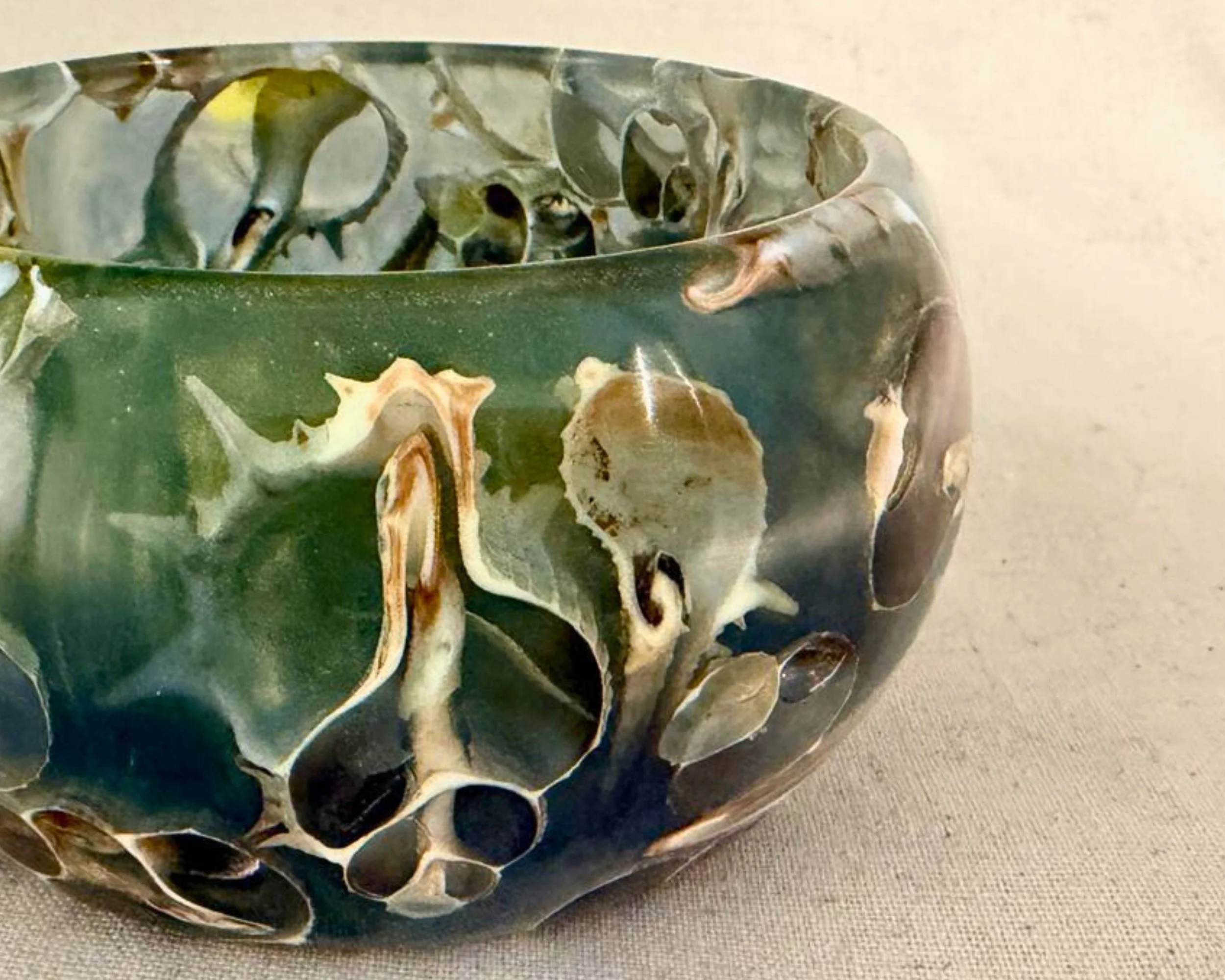 Close-up of green-blue epoxy vessel rim showing embedded real seashell fragments beneath glossy resin.