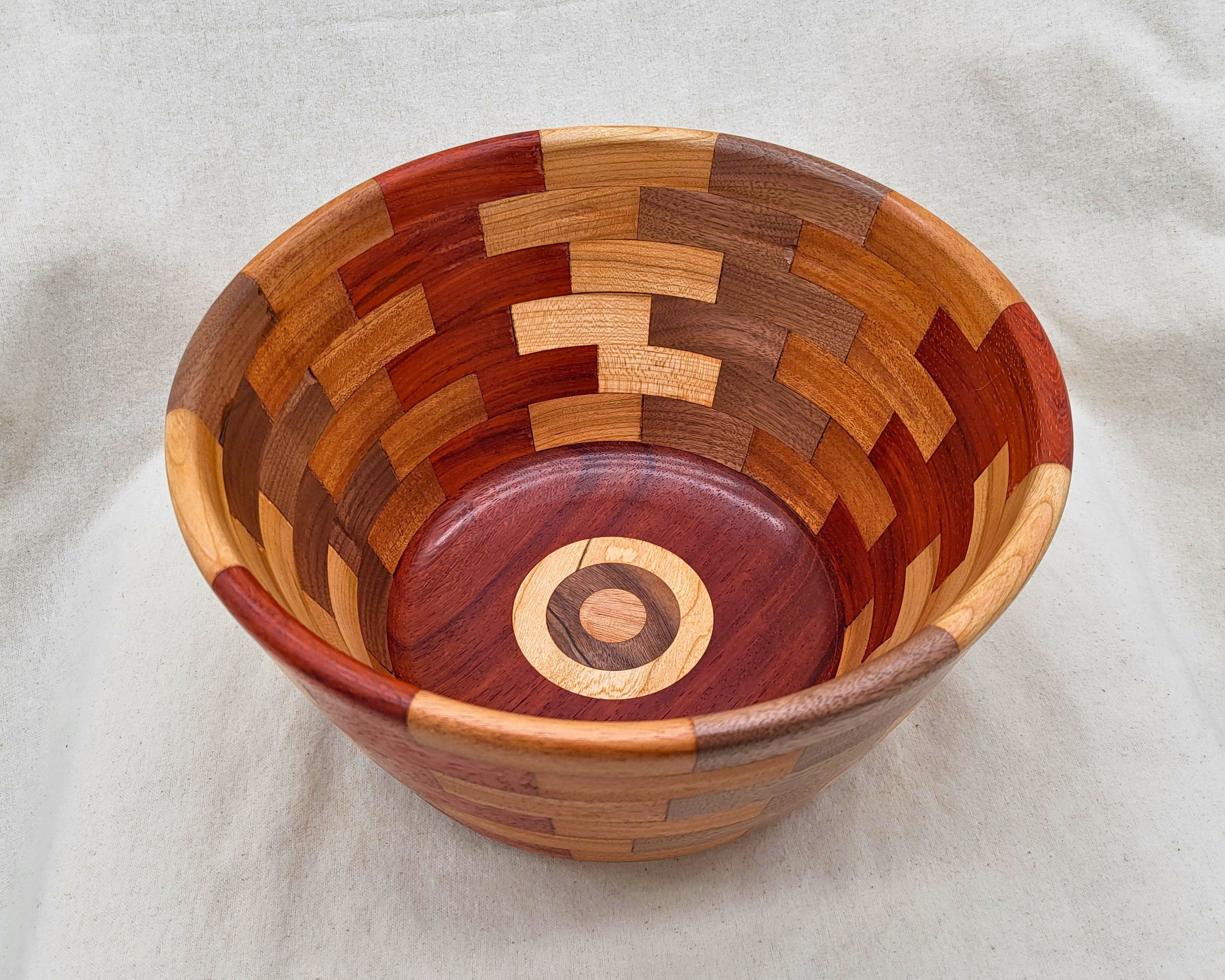 Interior view of a hand-turned segmented wood bowl by Treverk Woodturning, looking past the rim to concentric rings of red padauk, maple, mahogany, and walnut descending toward a layered medallion at the base. Sculptural decorative wood