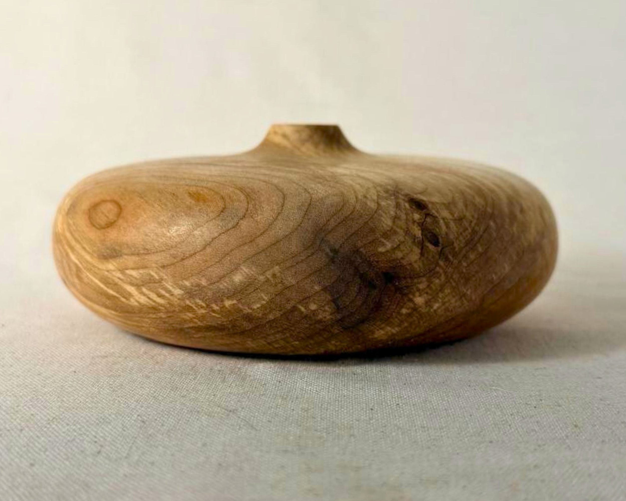 Side profile of the figured maple closed form vessel showing its low height, rounded body, and small top opening.
