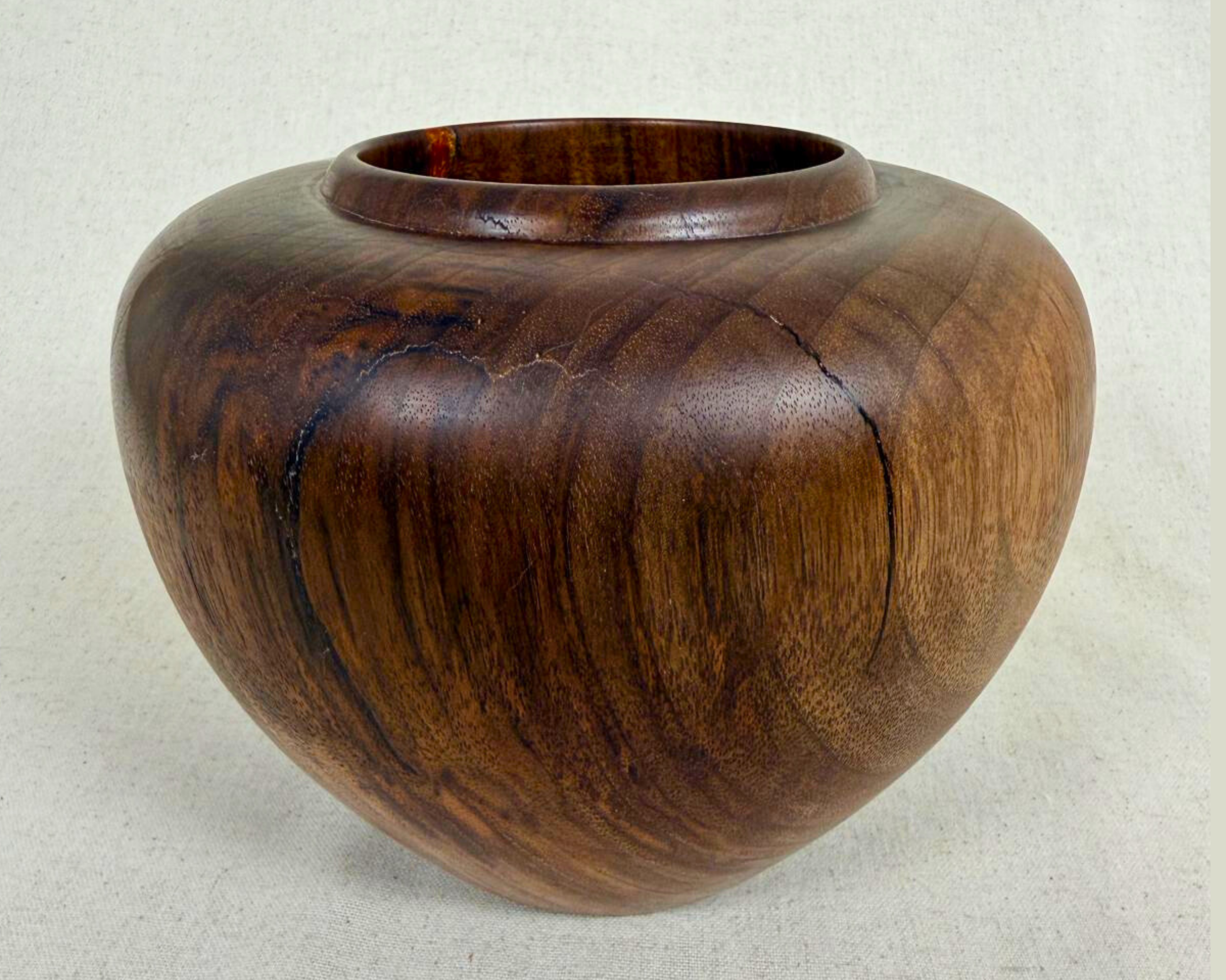 Front view of a hand-turned dark wood vessel with a low wide form, rounded shoulder, and visible natural crack lines across the surface.