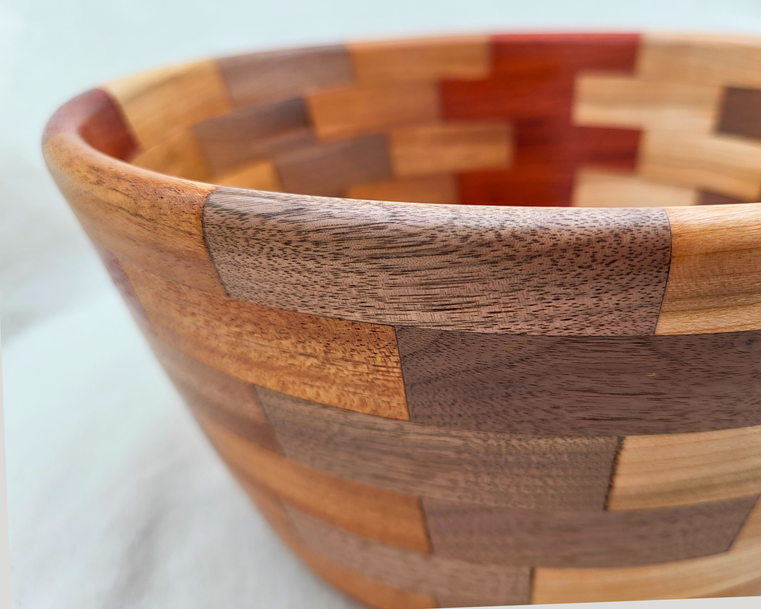 Close-up of the curved rim on a hand-turned segmented wood bowl by Treverk Woodturning, showing the transition between maple, walnut, and padauk blocks and the smooth satin finish. Sculptural decorative wood bowl.