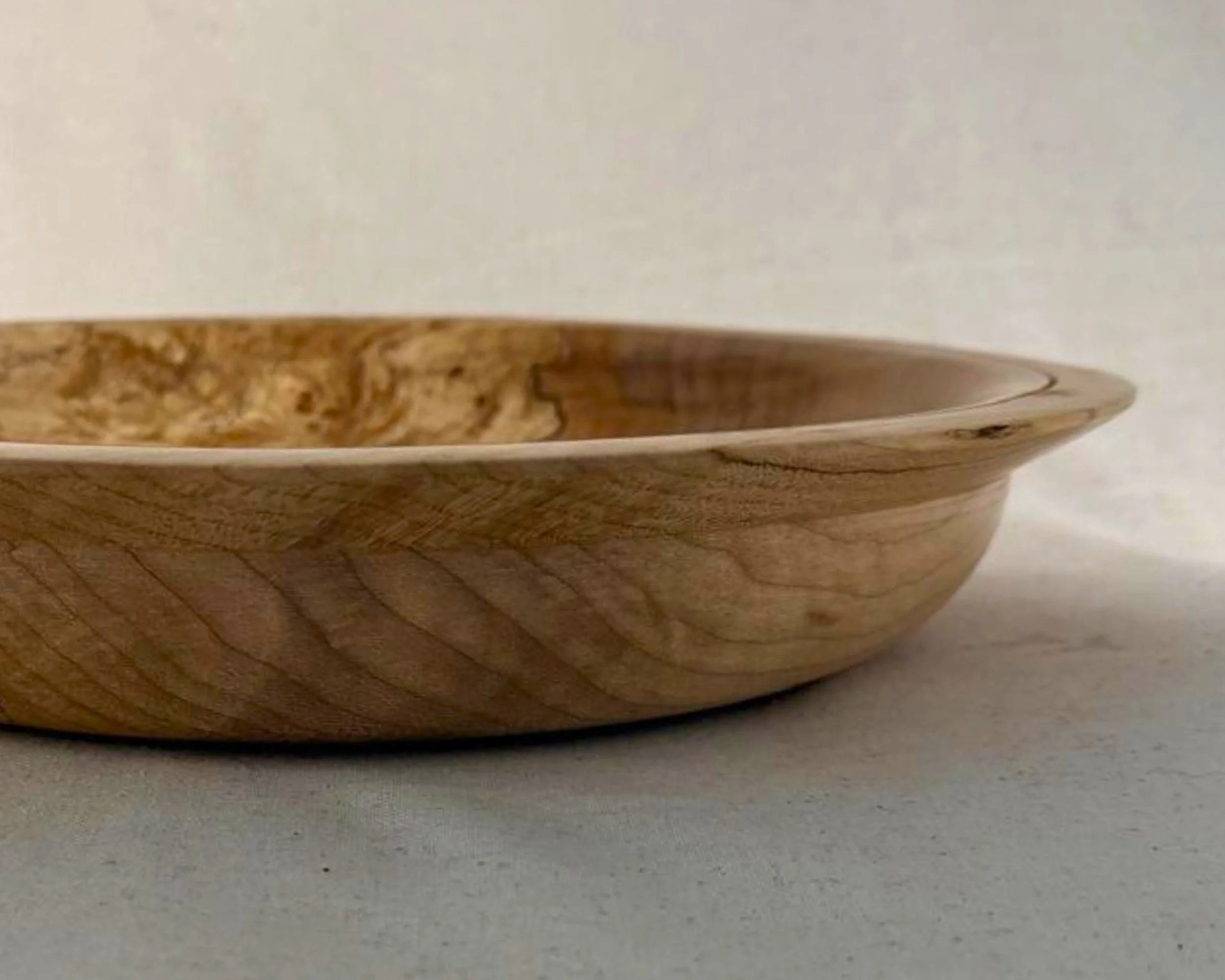 Close side profile of a shallow hand-turned wooden platter, wide flared rim, smooth curve, figured grain with spalted areas.