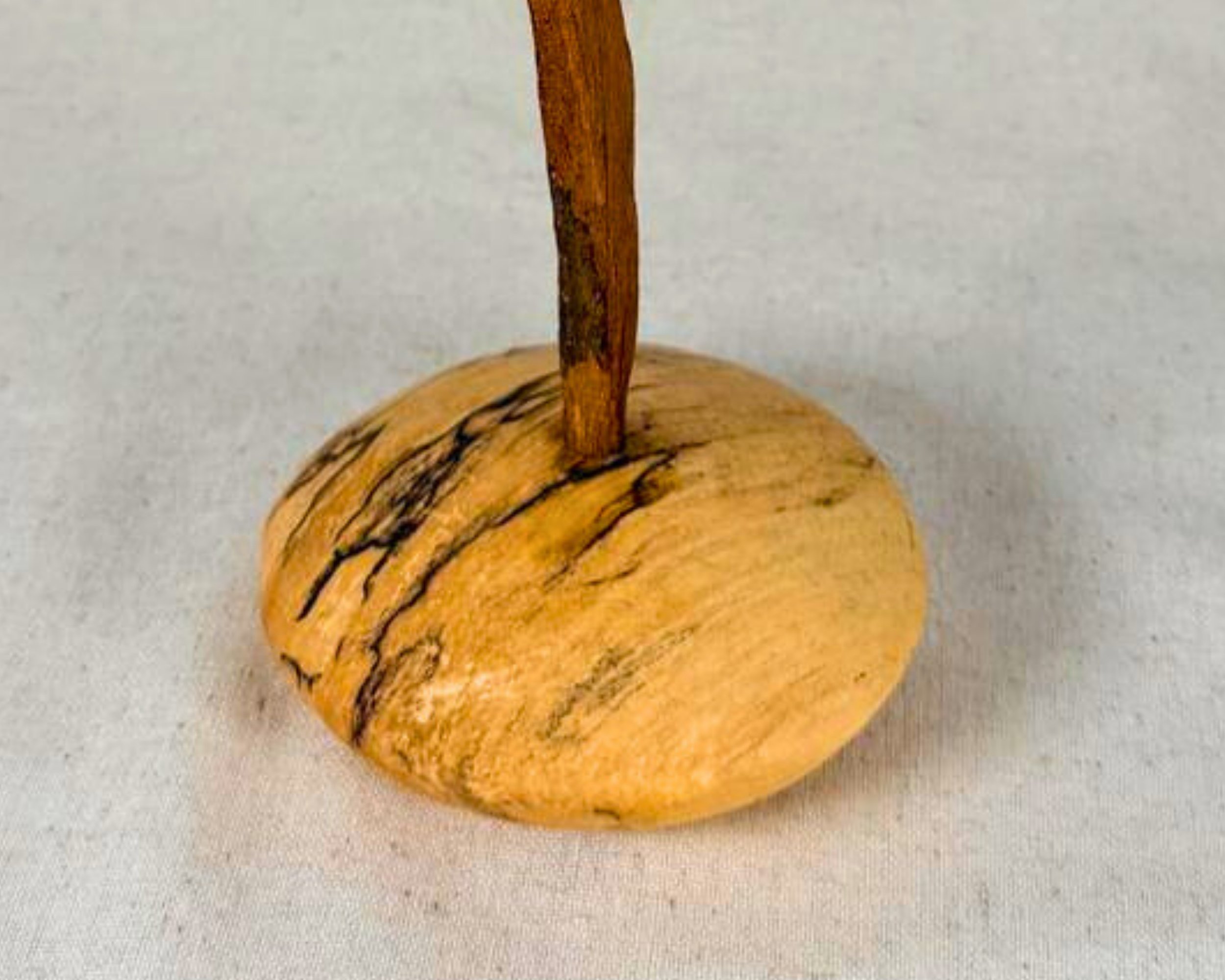 Close up of the turned spalted maple base showing natural black spalting lines and the driftwood stem emerging from the center.