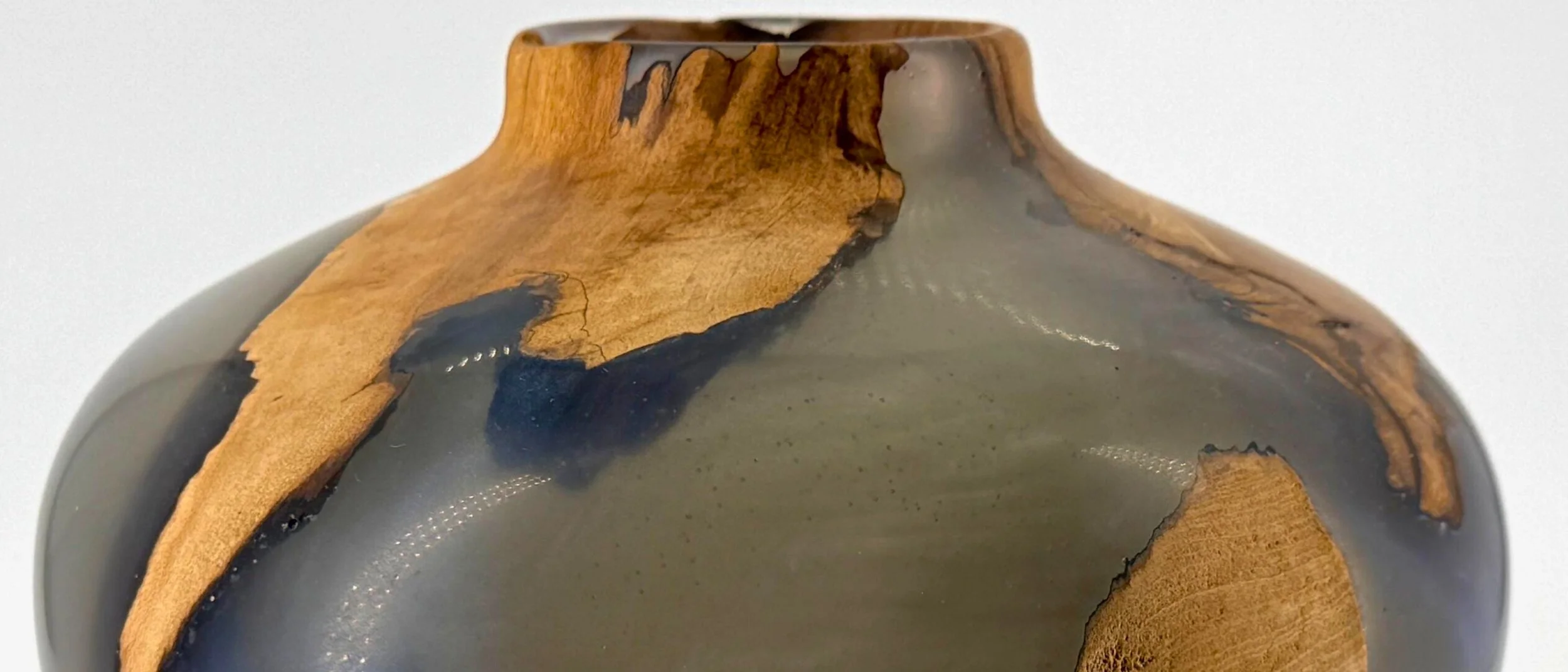 Close-up of a wood and epoxy turned vessel of blues and grays, reflecting light.