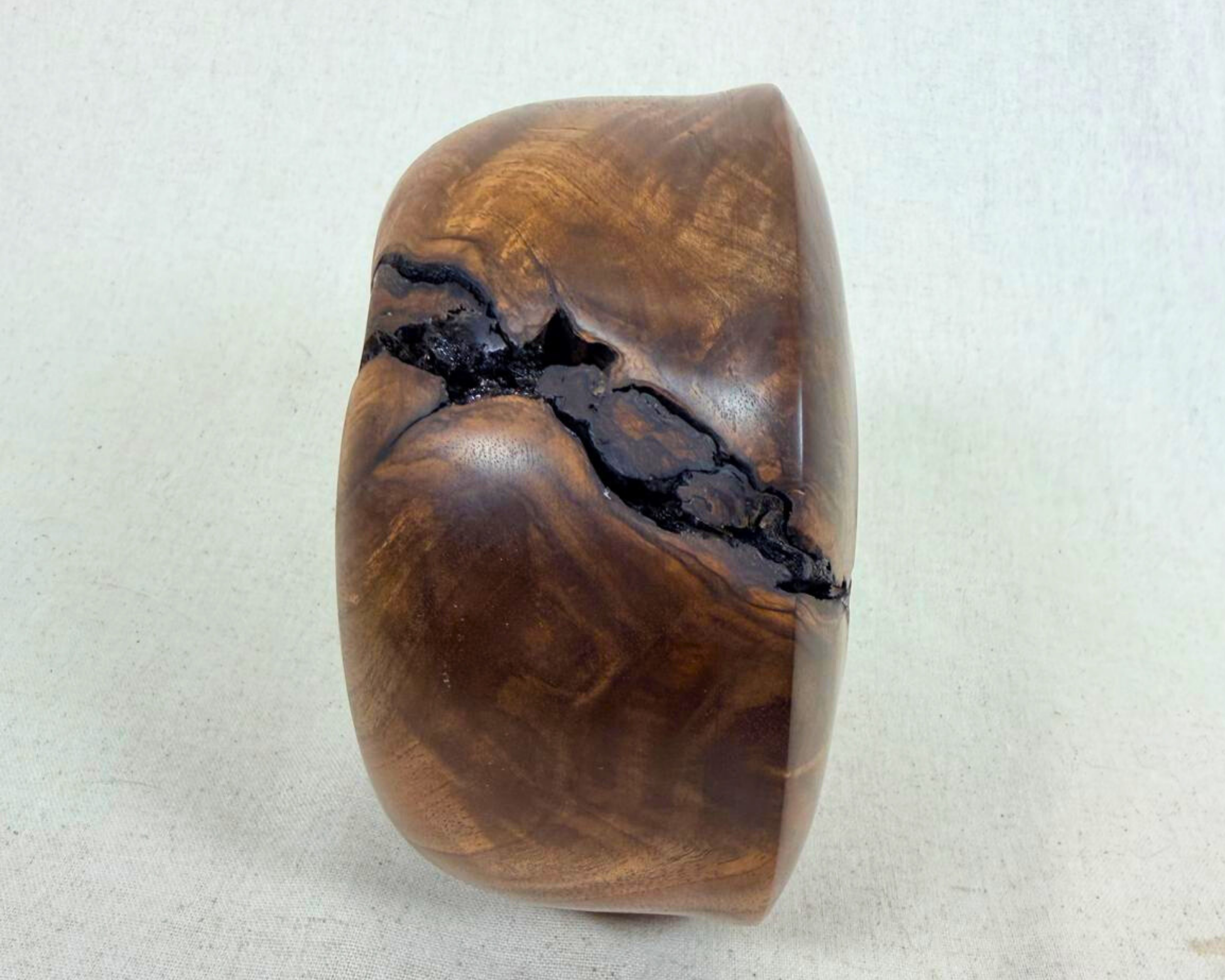 Side profile of a walnut vessel showing its low sculptural silhouette, rounded mass, and a natural fissure line cutting across the form.