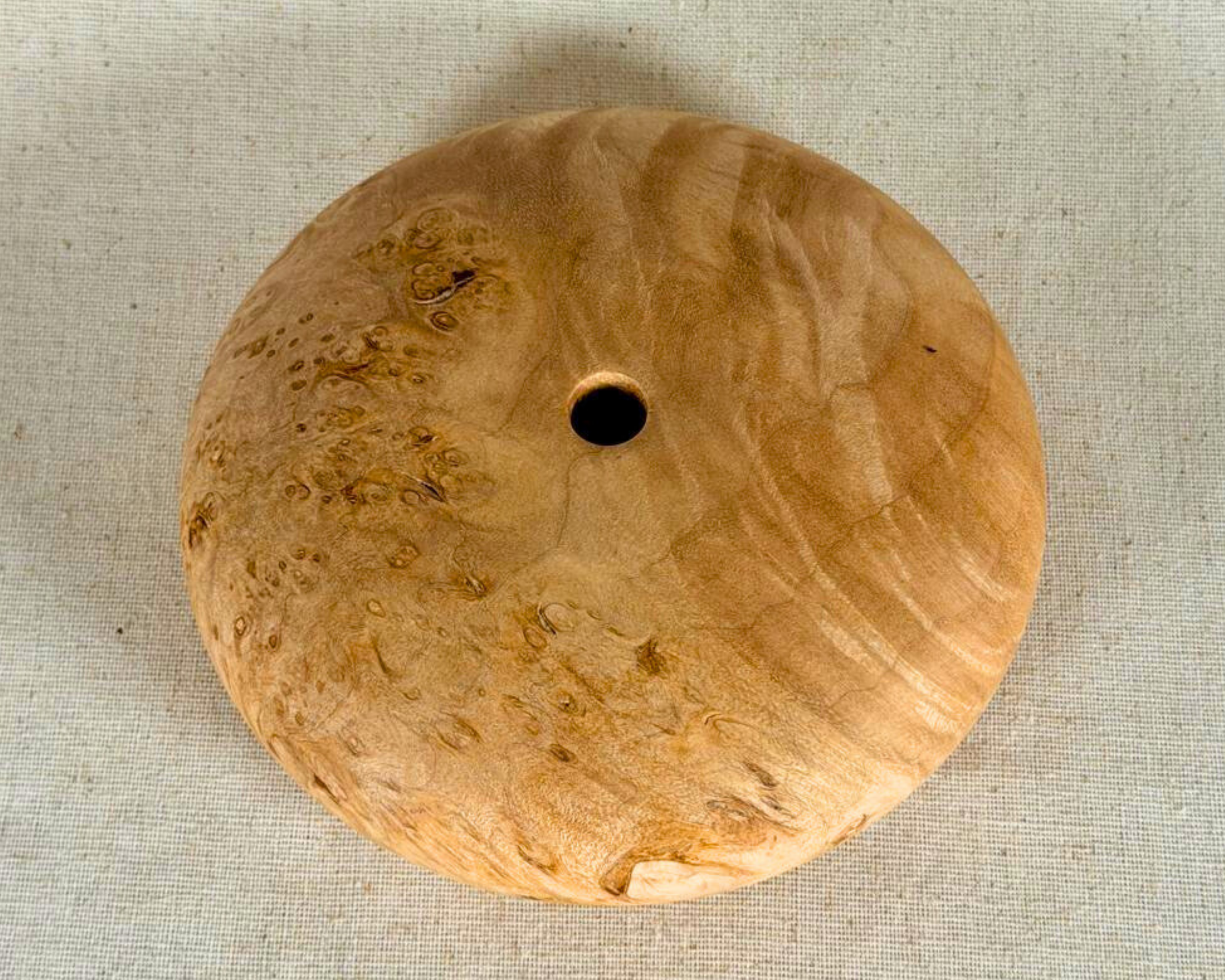 Top view of the maple burl form showing the small opening centered within swirling pale figure and clustered burl patterning.