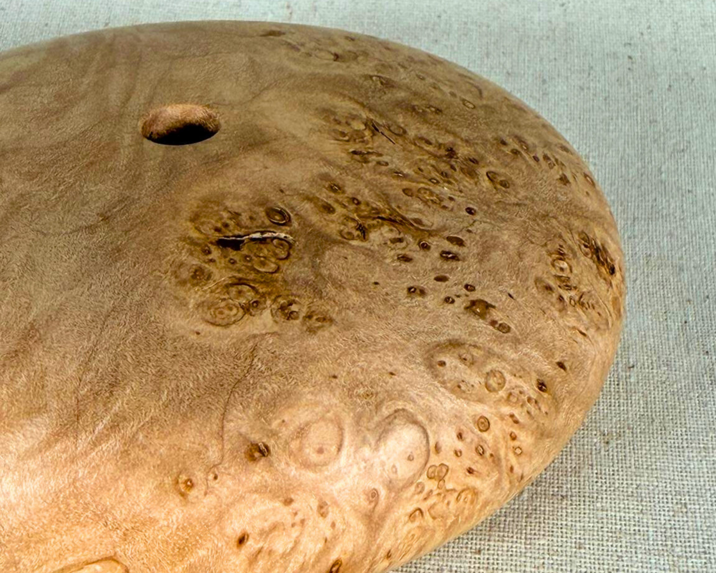 Close-up of the maple burl surface showing dense burl eyes, soft tonal variation, and natural figuring near the opening.