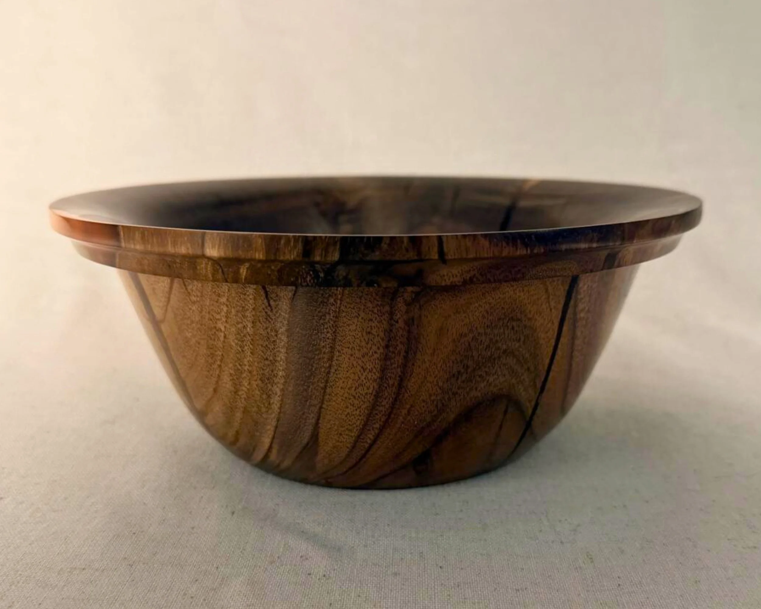 Side profile of a claro walnut bowl showing low, wide form and rim thickness with red epoxy accents visible.