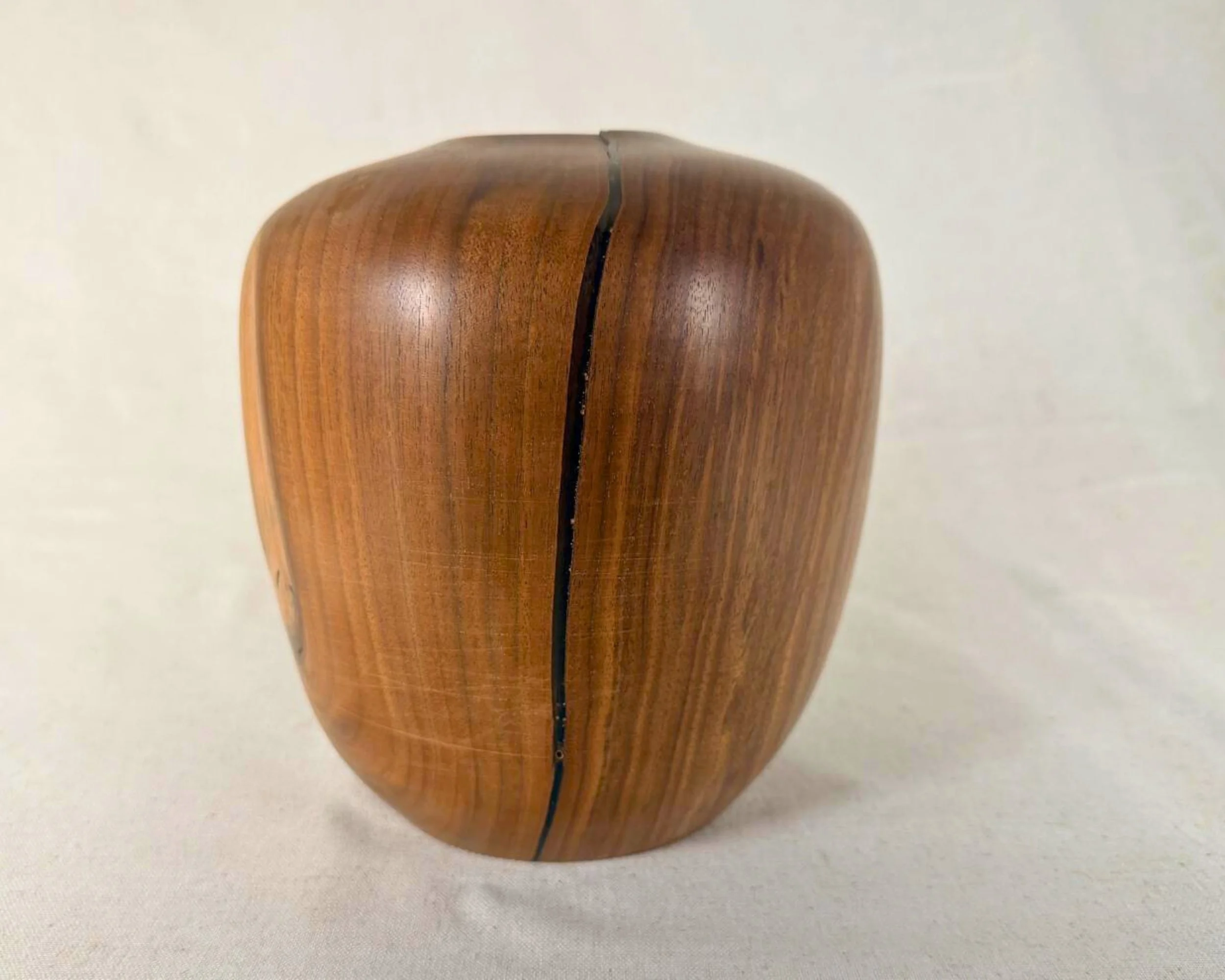 Side profile of walnut vessel highlighting a vertical black epoxy-filled seam line and compact, rounded silhouette.