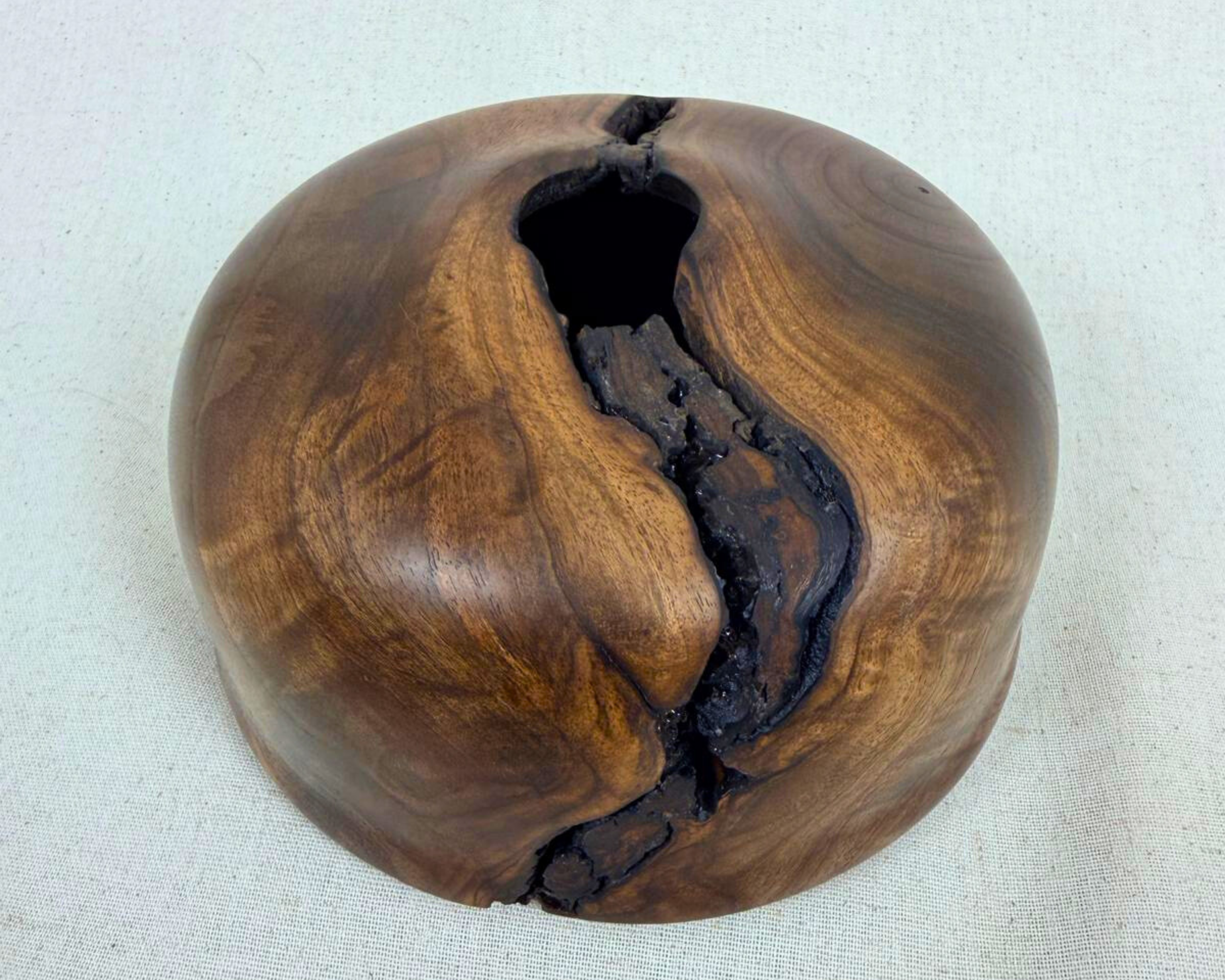 Hero image of a hand-turned walnut vessel with rich swirling grain, asymmetrical profile, and a dark natural fissure running diagonally across the piece.