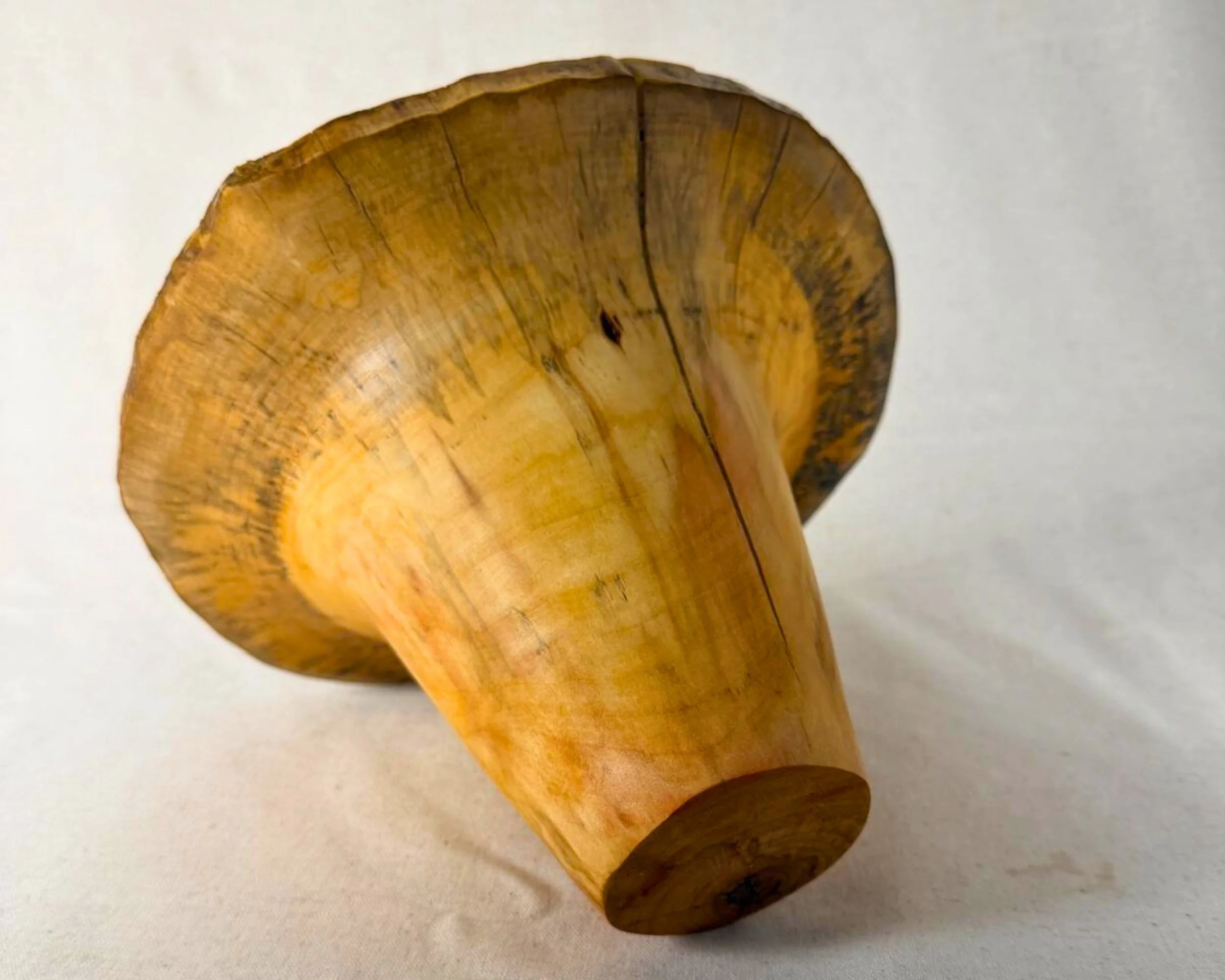 Angled view of the vessel lying on its side, showing the tapered base and maple grain movement.