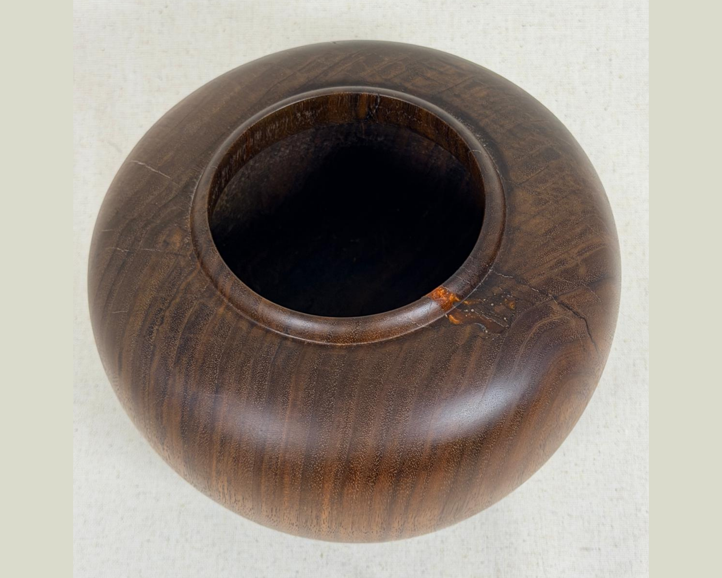 Top view of a hand-turned dark wood vessel with a wide circular opening, visible flowing grain, and a small amber-toned natural inclusion near the rim.