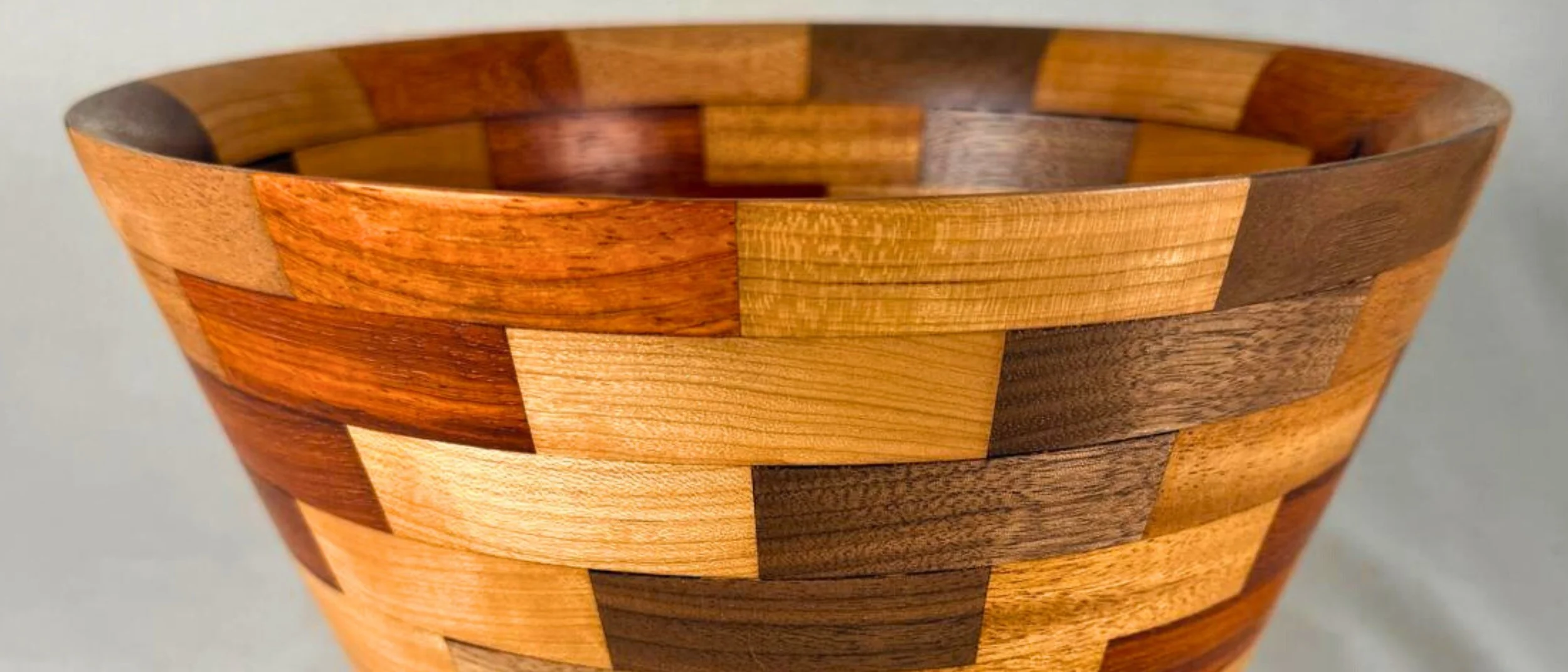 Close-up of a handturned segmented vessel with multicolored rectangular pieces of wood assembled in a pattern.