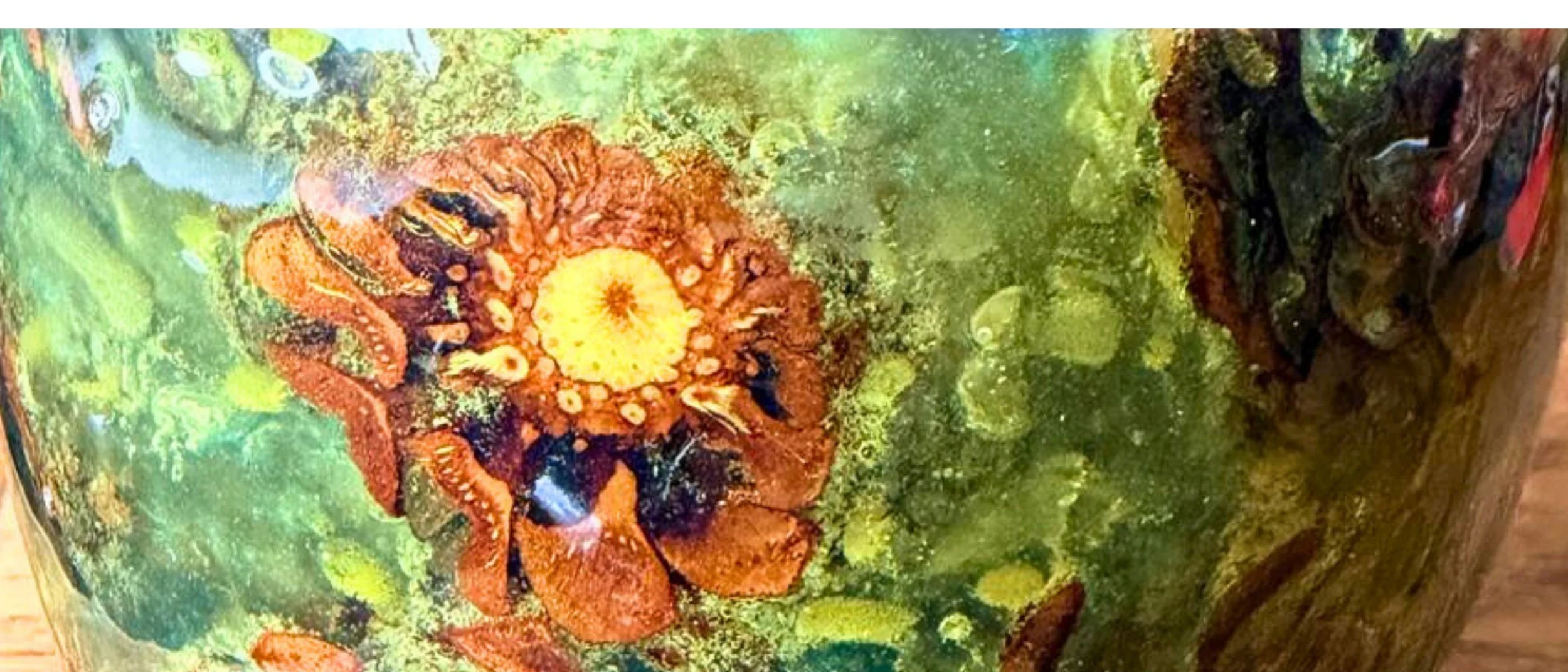 Close-up of a hand-turned epoxy vessel in which pine cones are suspended in green and blue resin.