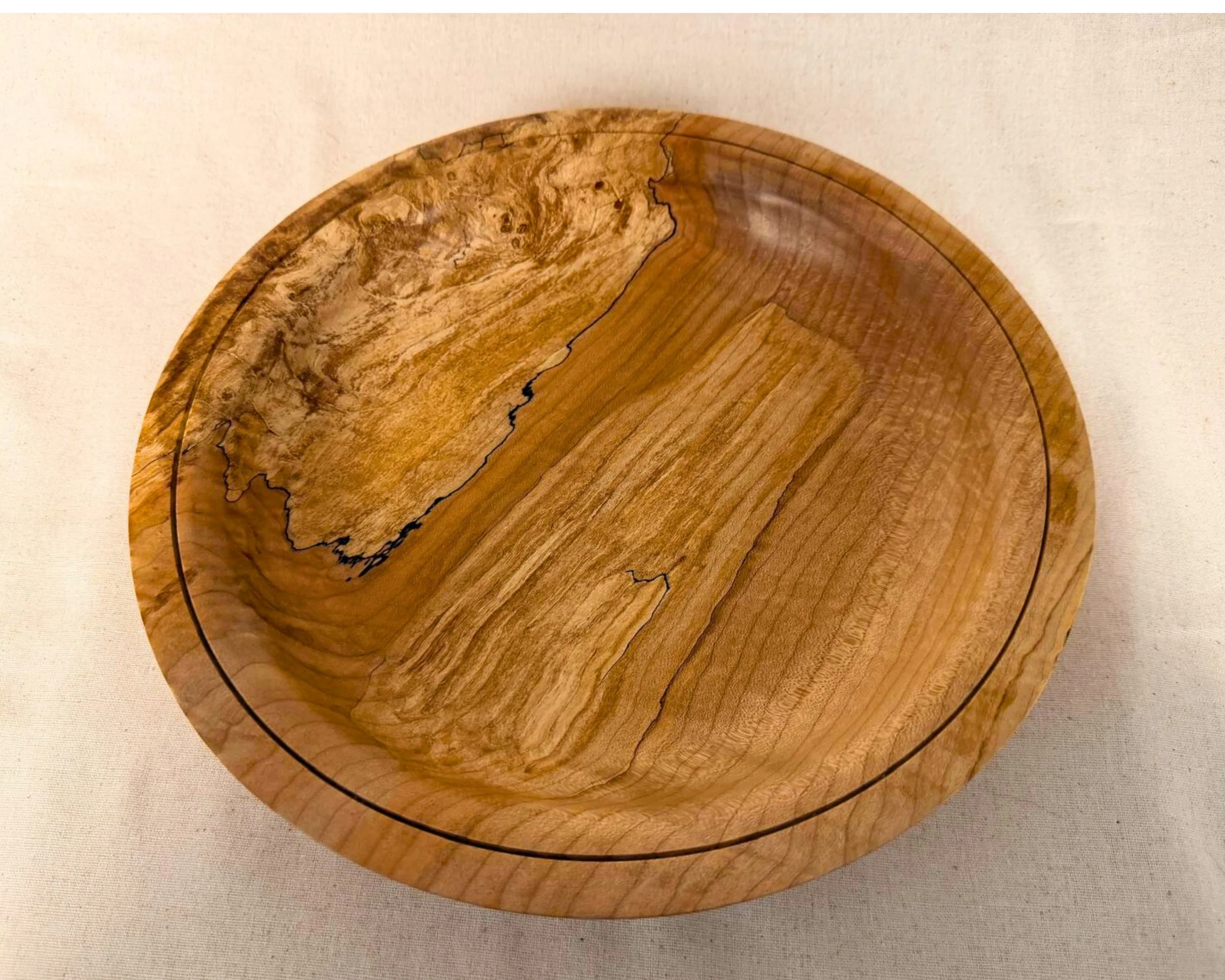 Top view of a hand-turned wooden platter, spalted grain pattern with dark spalt lines, thin circular groove detail near the rim.
