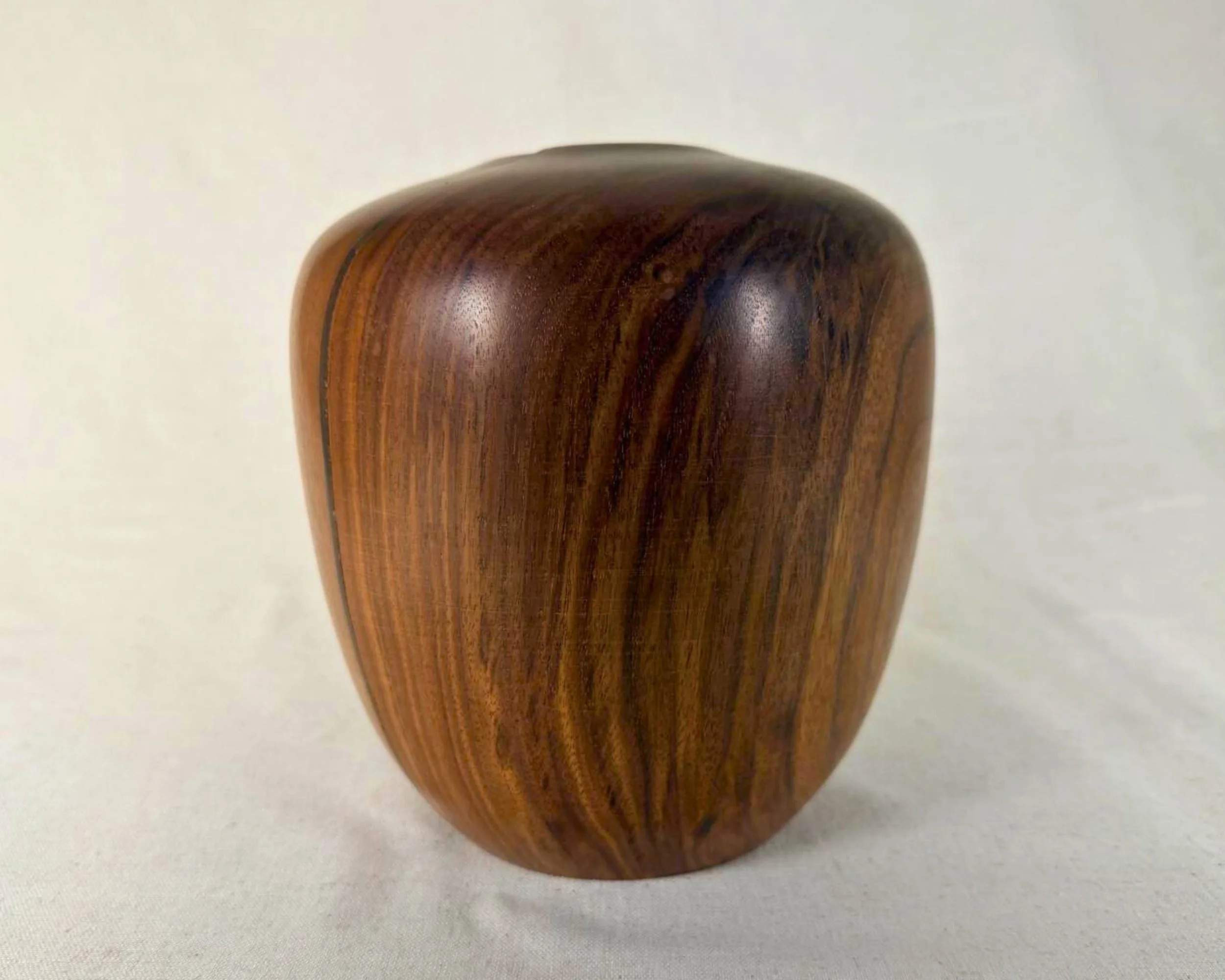 Three-quarter view of walnut vessel showing sweeping grain movement and a clean rimless top edge.