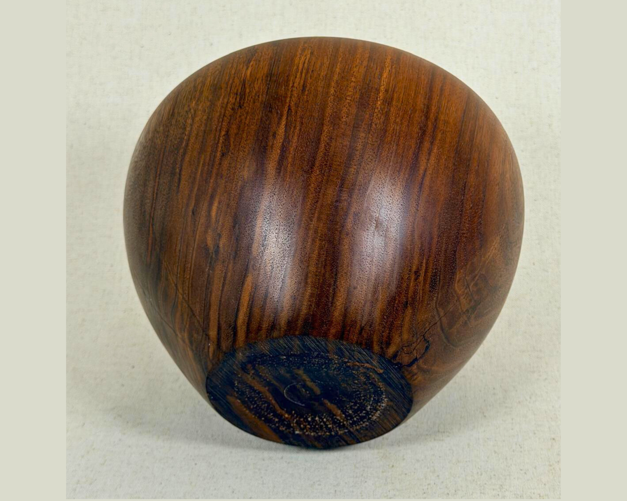 Underside view of a hand-turned dark wood vessel showing the rounded base, dark foot, and continuous vertical grain patterns.