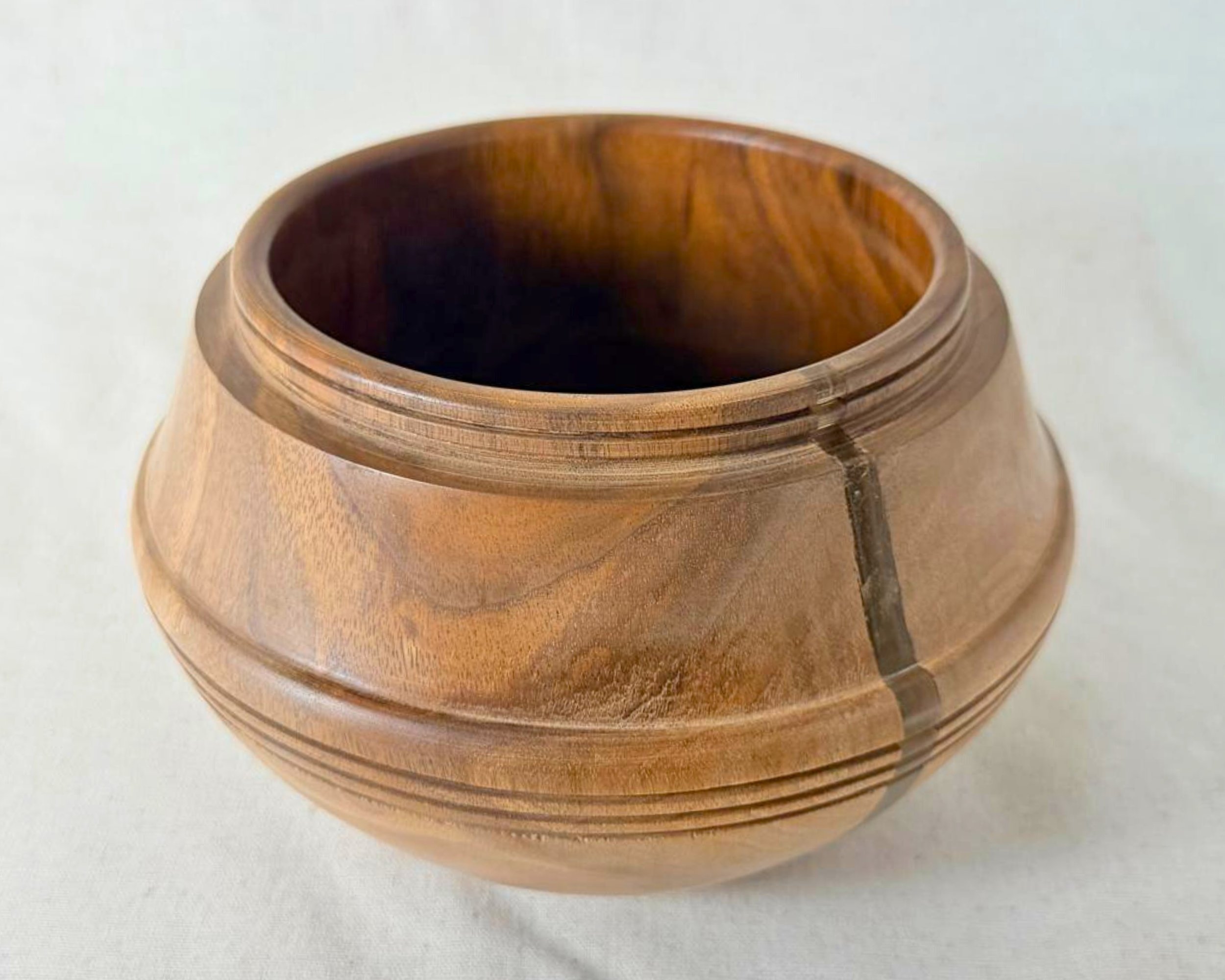 Front view of walnut bowl with rounded silhouette, banded rings, and a neutral epoxy accent on light fabric.