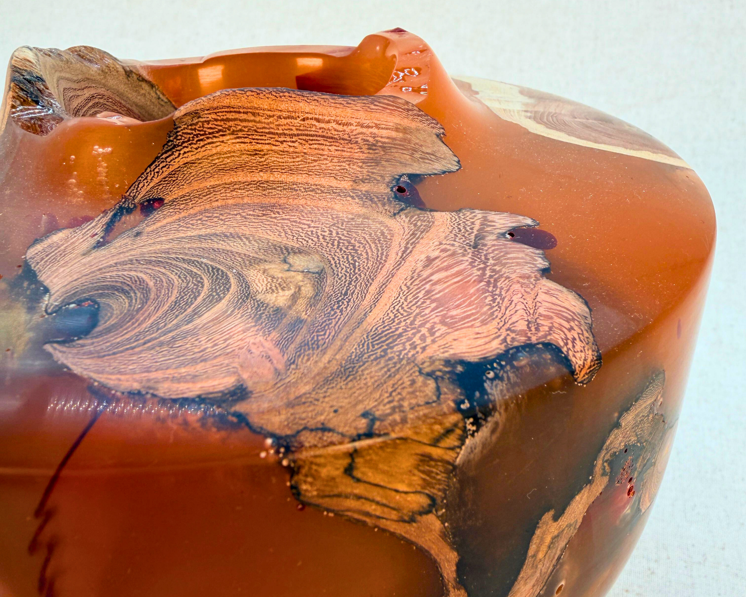 Close-up of a hand-turned driftwood and ochre amber epoxy vessel showing exposed wood inclusions, sculptural rim contours, and translucent resin detail in a one-of-a-kind art vessel.