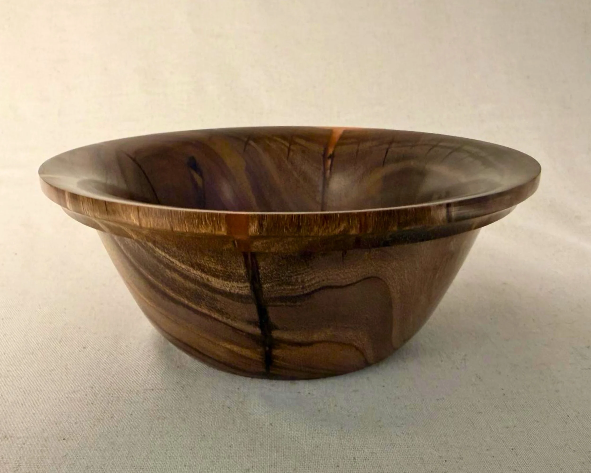 Claro walnut bowl with red epoxy highlights along the rim, shown in a wide three-quarter view.