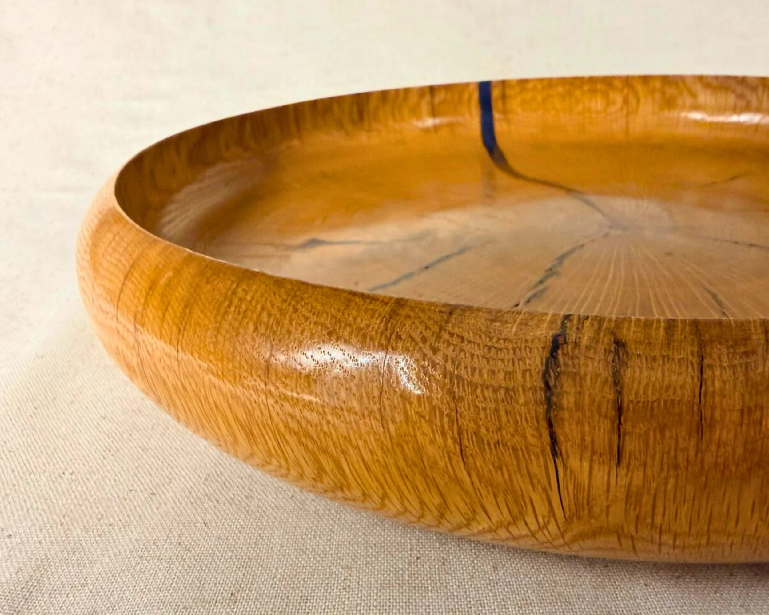 Side profile of a reclaimed oak platter highlighting the thick rounded rim and glossy finish.