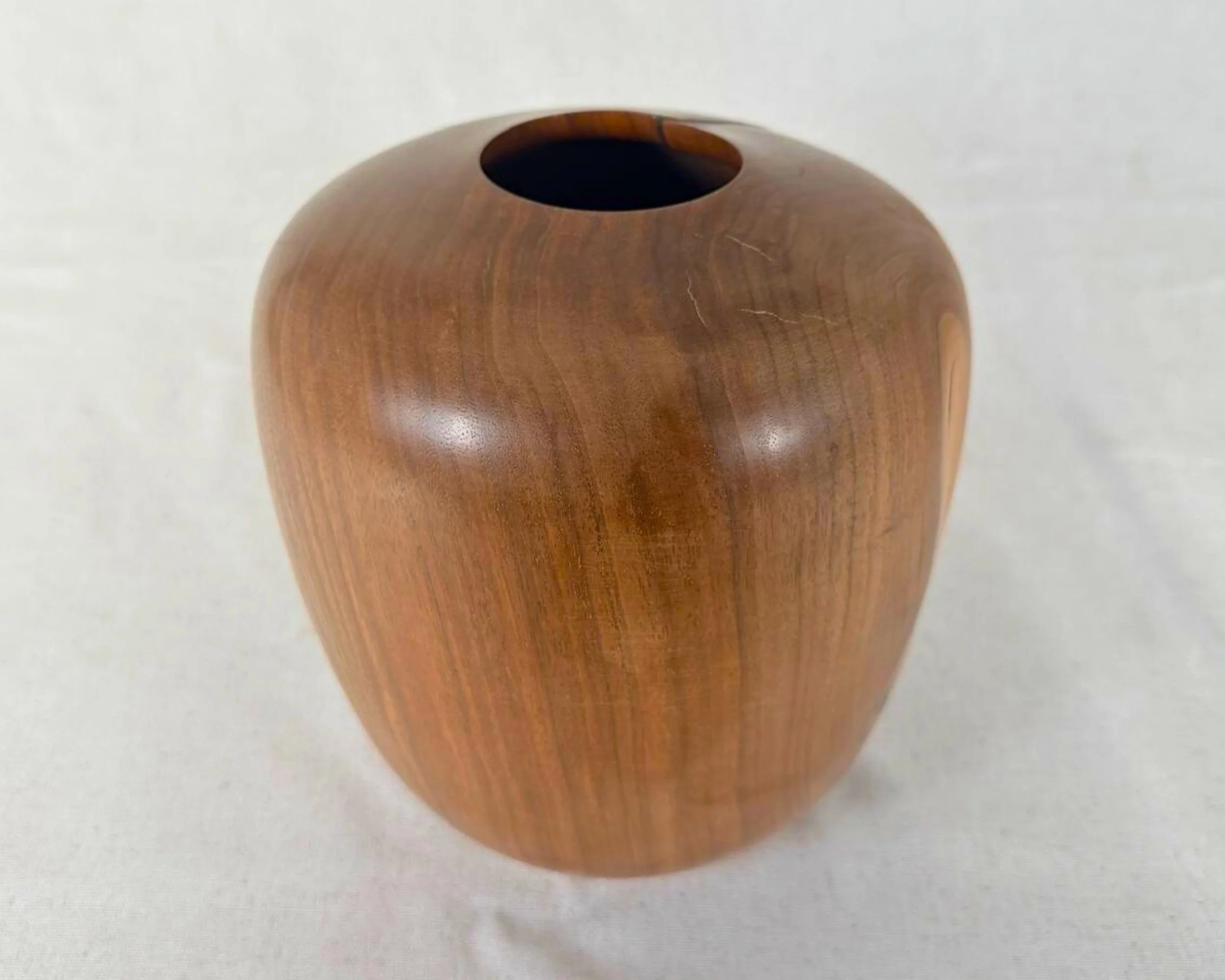 Hand-turned walnut vessel with rimless opening, rounded form, and visible grain pattern, photographed from a front angle.