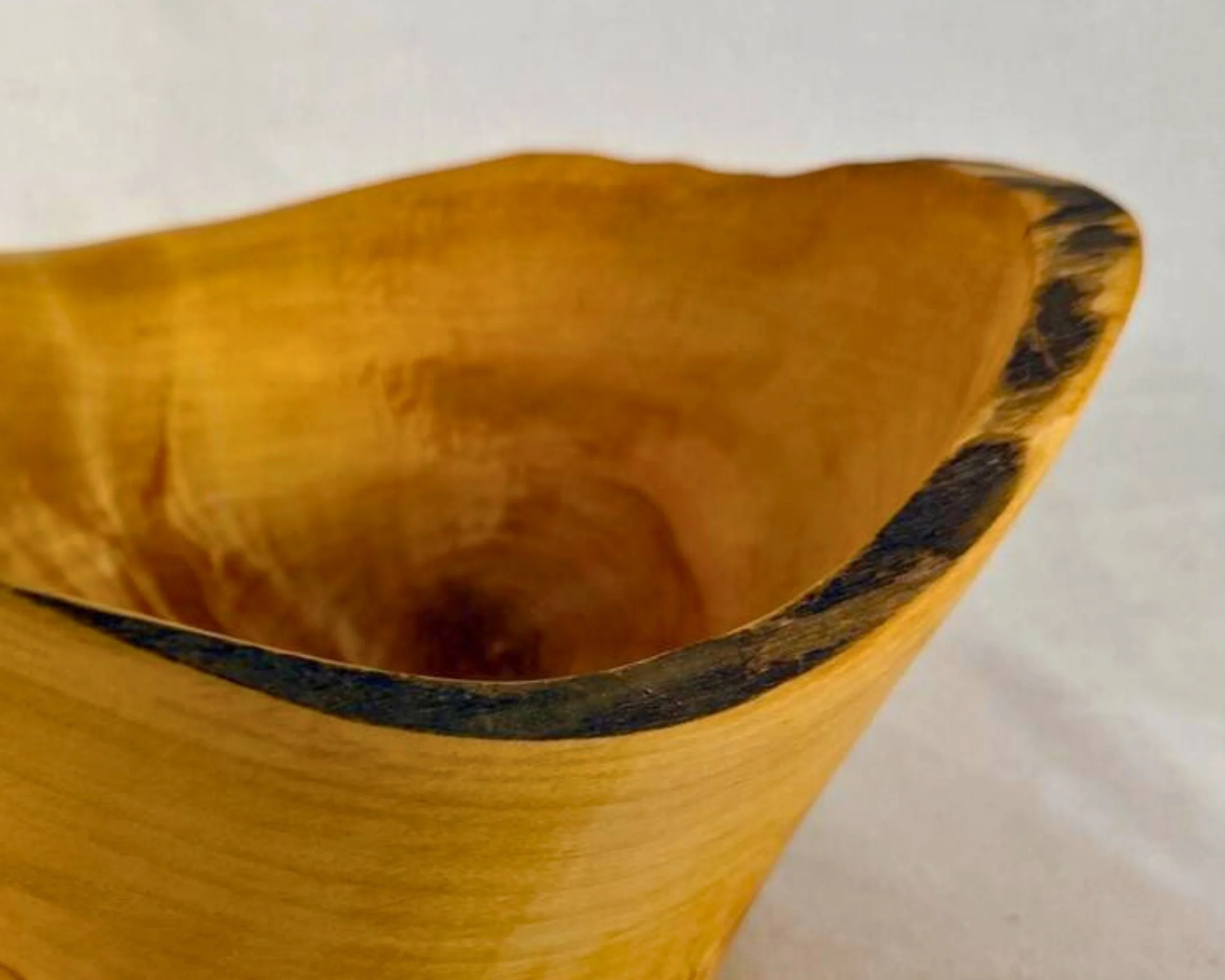 Close up of natural edge rim showing dark bark line against golden pine.