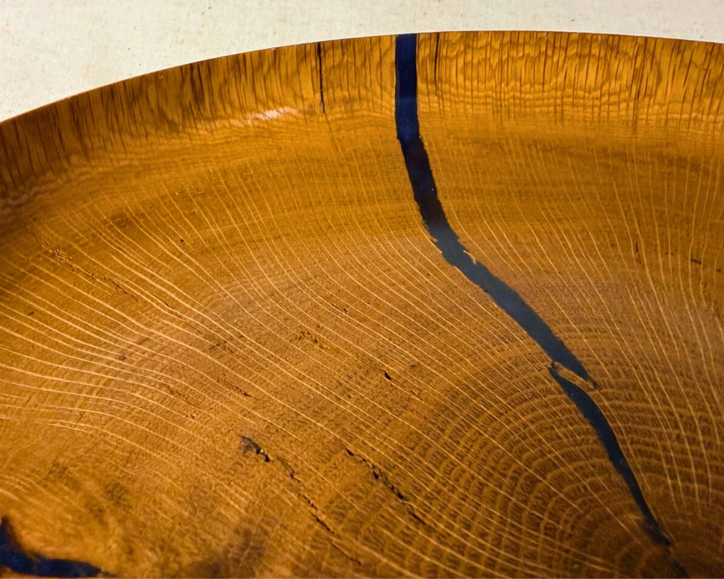 Close-up of reclaimed oak growth rings intersecting with a dark blue epoxy-filled void on a glossy platter surface.