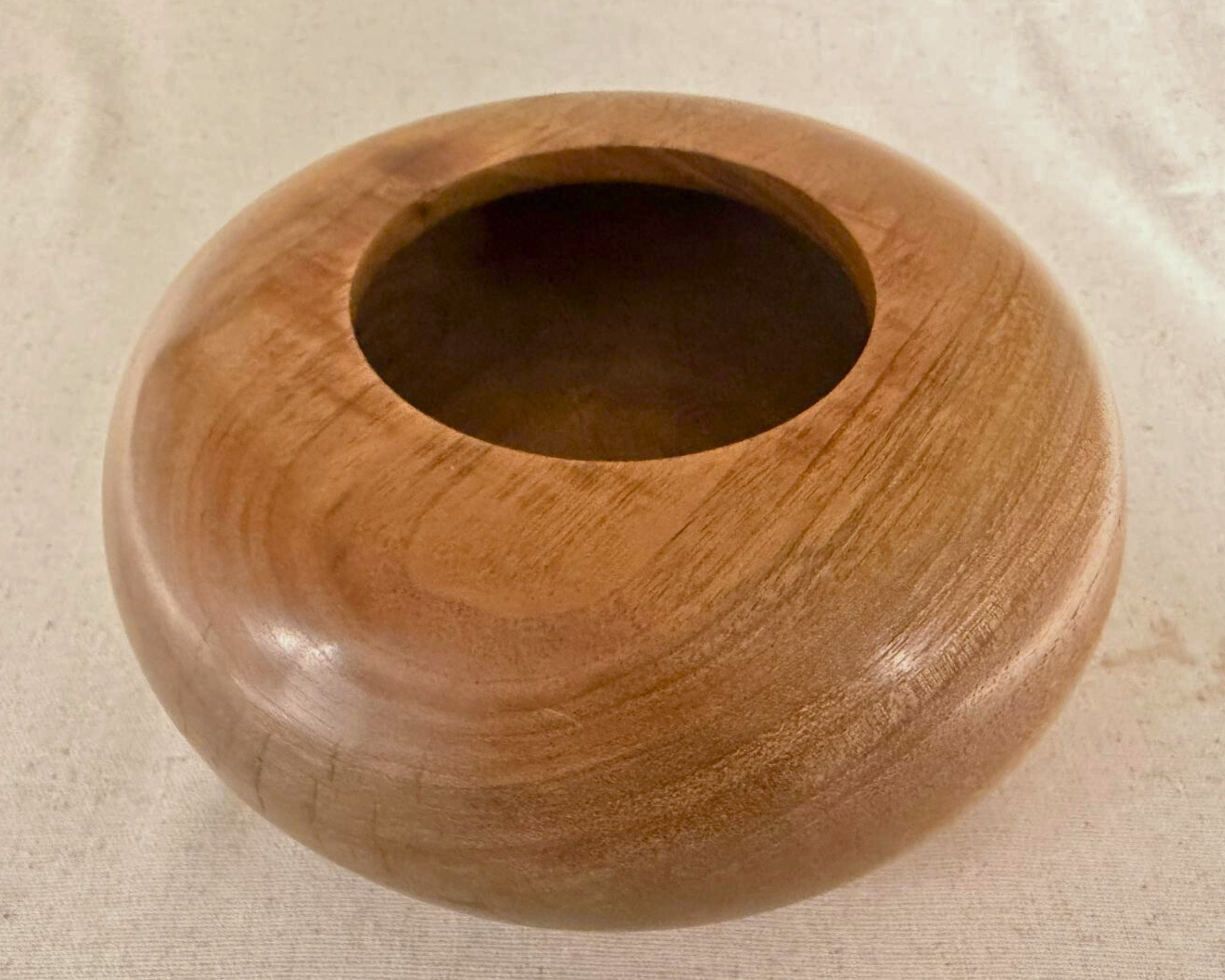 Angled top view of claro walnut closed form vessel emphasizing the rim, opening, and rounded shoulder in warm chocolate tones.