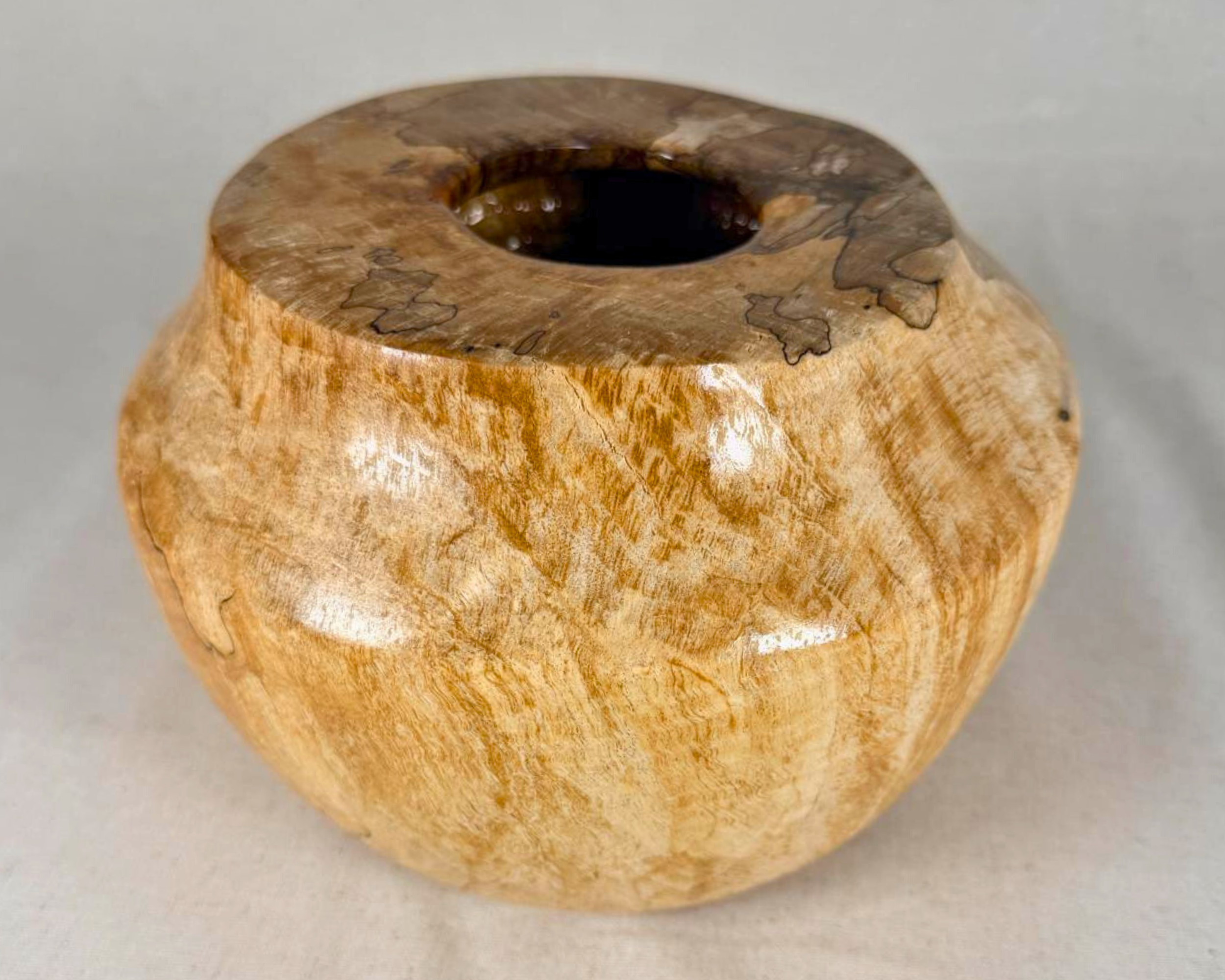 Spalted maple vessel photographed from the front at a slight angle, showing the rounded silhouette, small opening, and soft contrast between creamy maple and dark spalting.