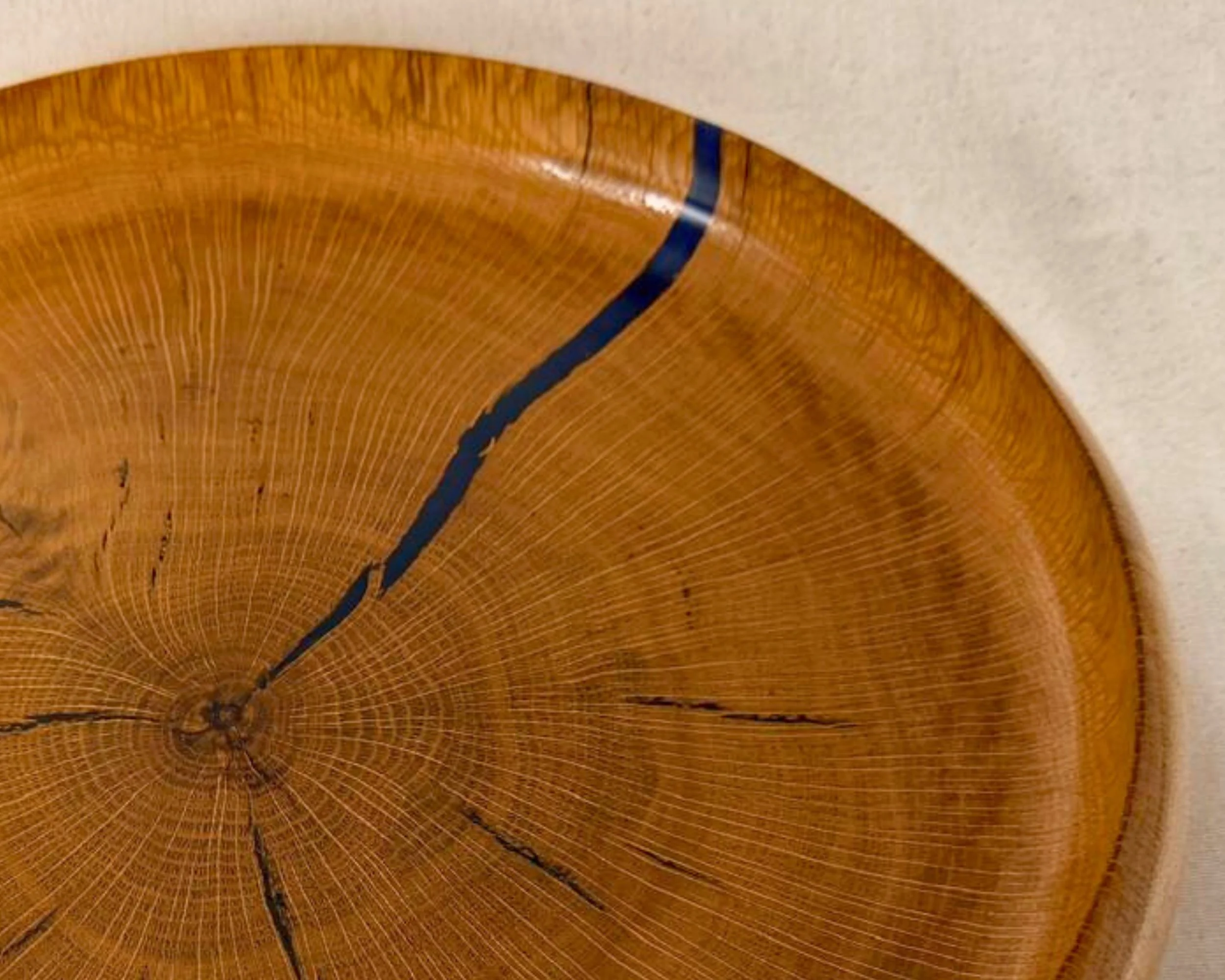 Close-up of the platter rim on reclaimed oak with dark blue epoxy in a natural split and a glossy finish.