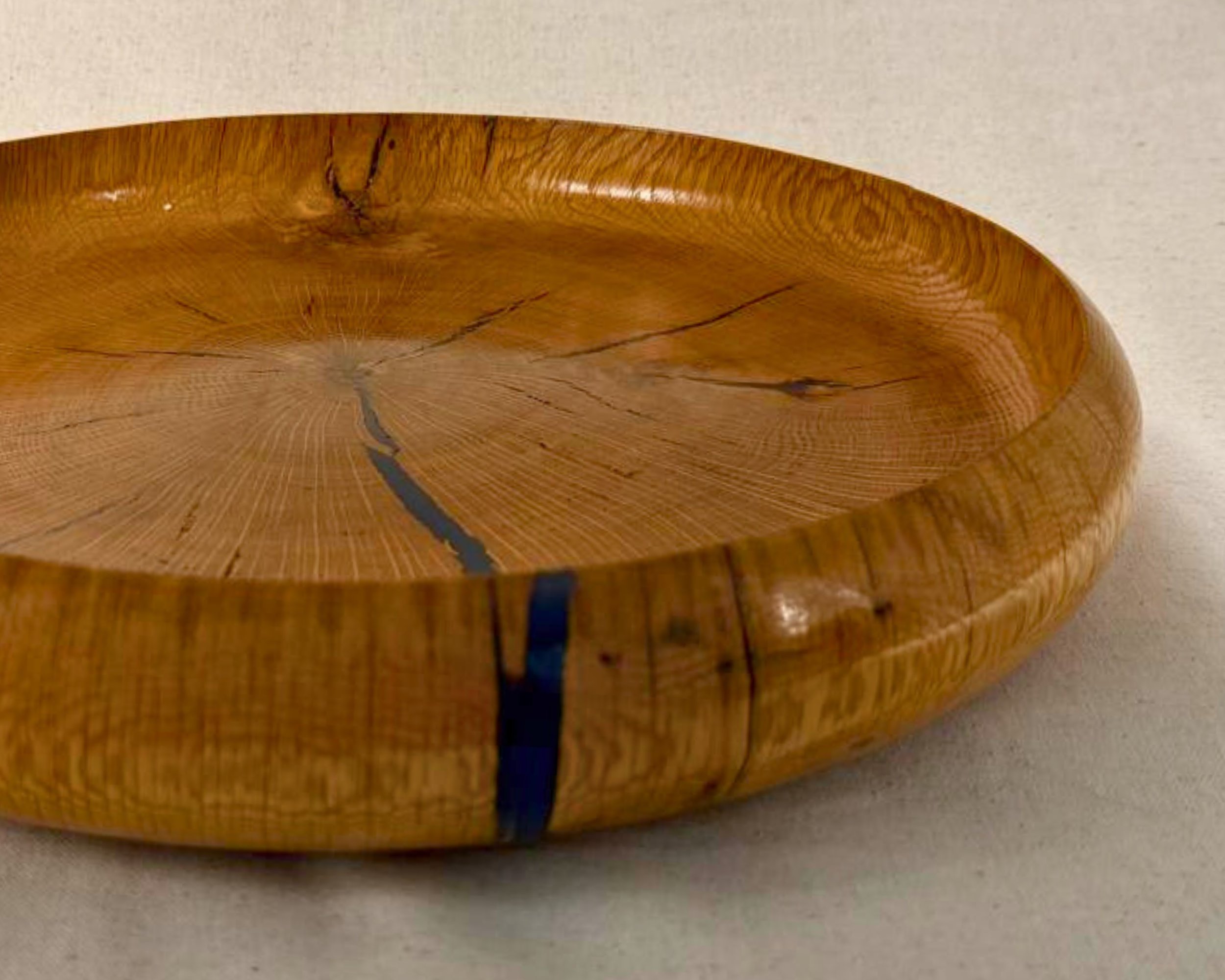 Angled close-up of a reclaimed oak platter with dark blue epoxy filling natural voids and a glossy finish.