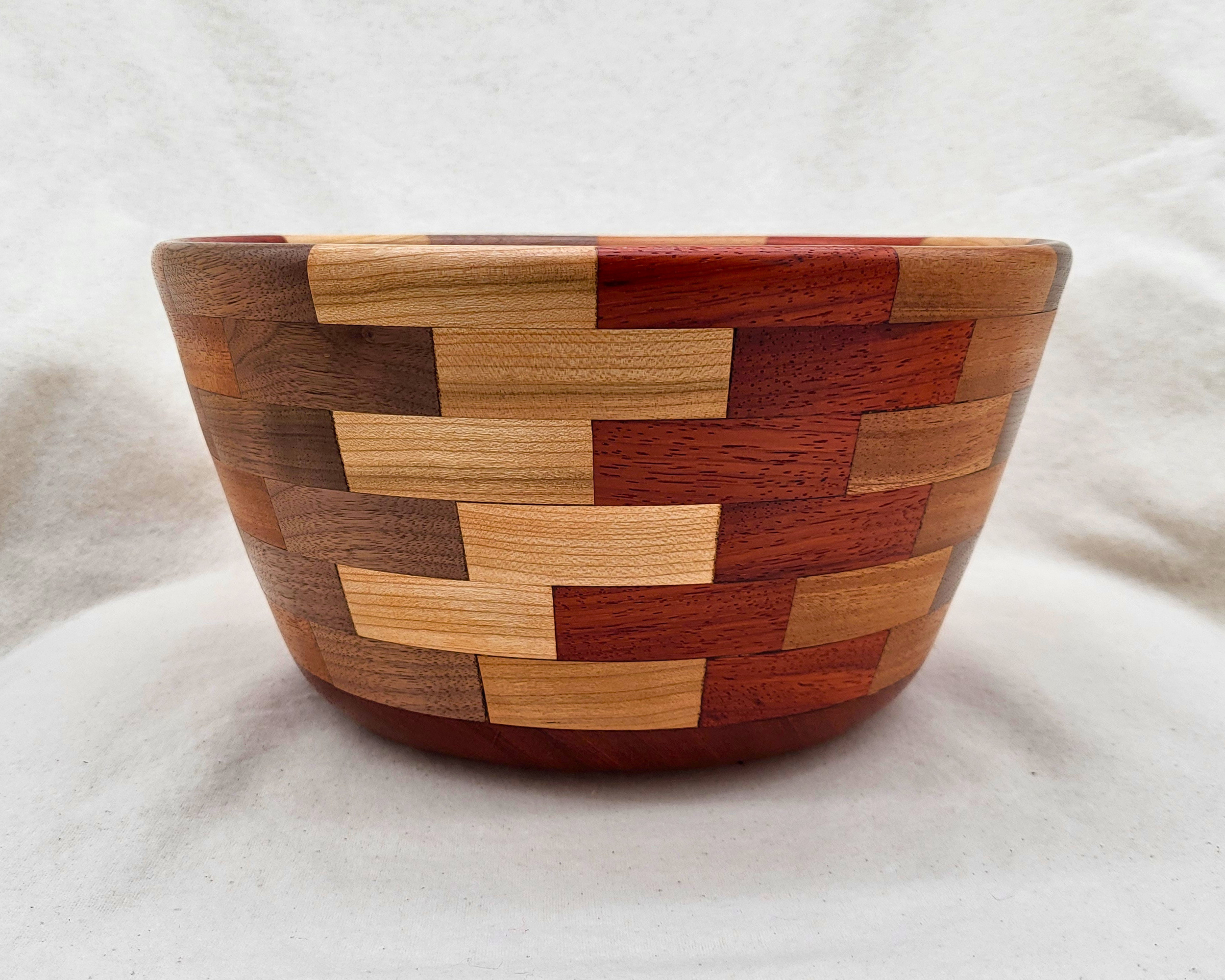 Profile view of a hand-turned padauk and walnut segmented bowl by Treverk Woodturning, showing the curving inward rim, the soft round base, and the running-bond pattern of contrasting hardwoods across the body. Sculptural wood bowl.