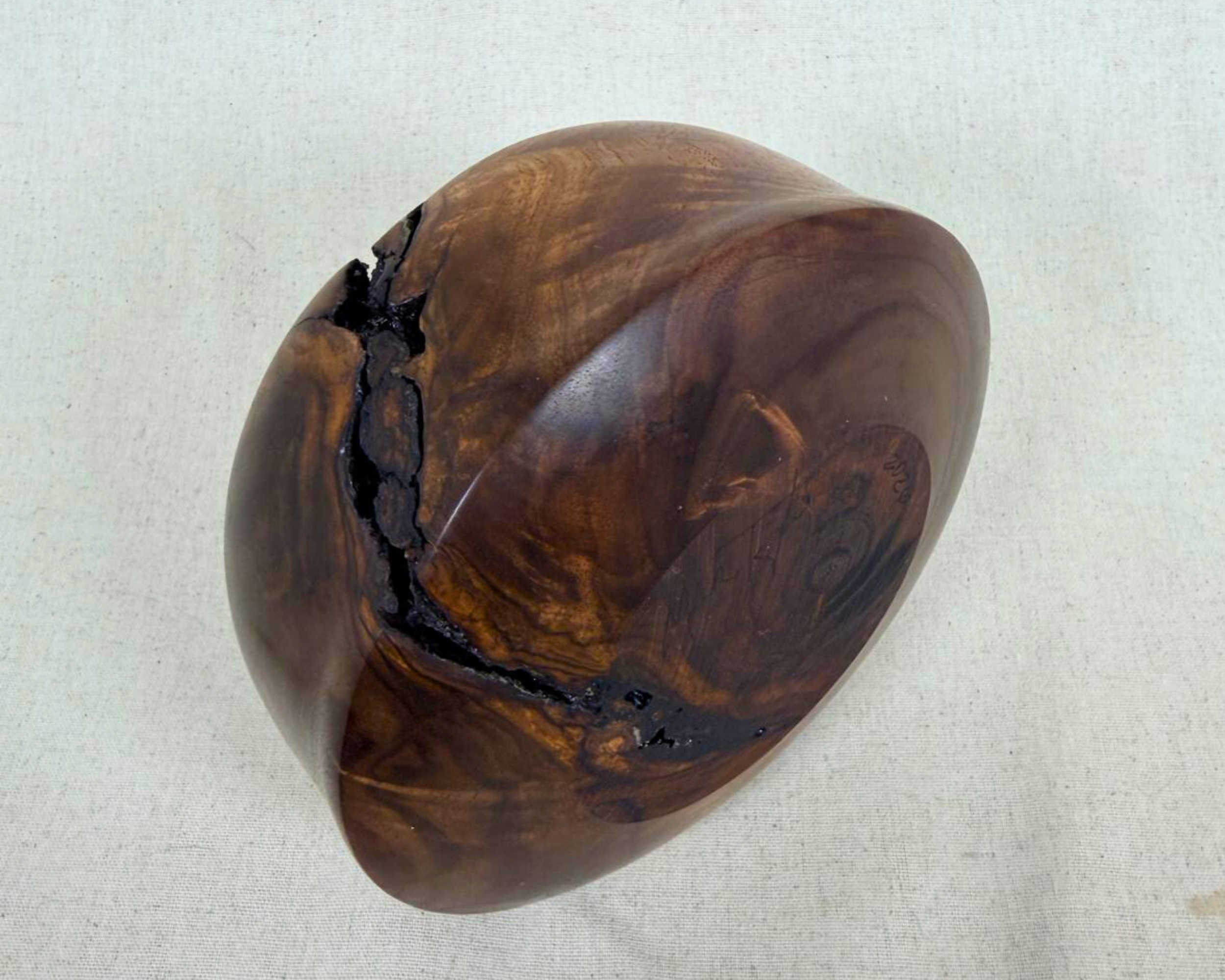 Underside view of a walnut vessel with rounded form, visible growth-ring center, and a long natural void opening crossing the upper edge.