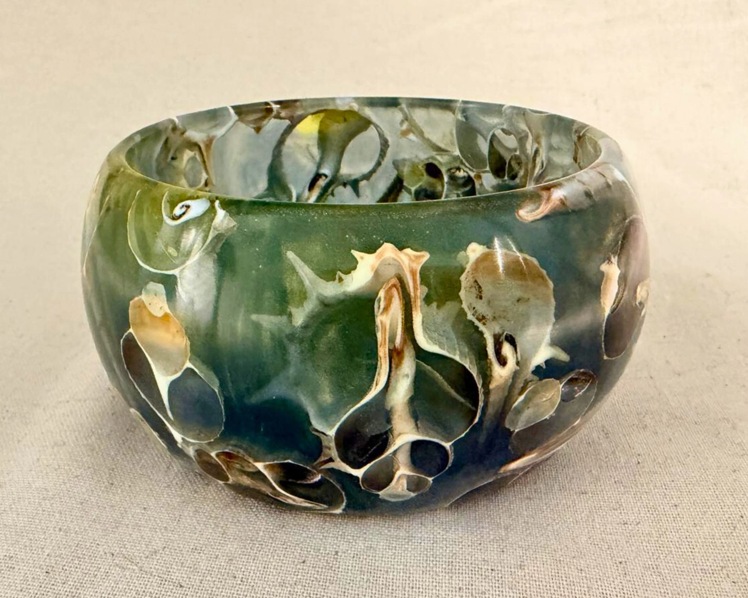 Full view of seashell and epoxy vessel in green-blue resin on neutral background.