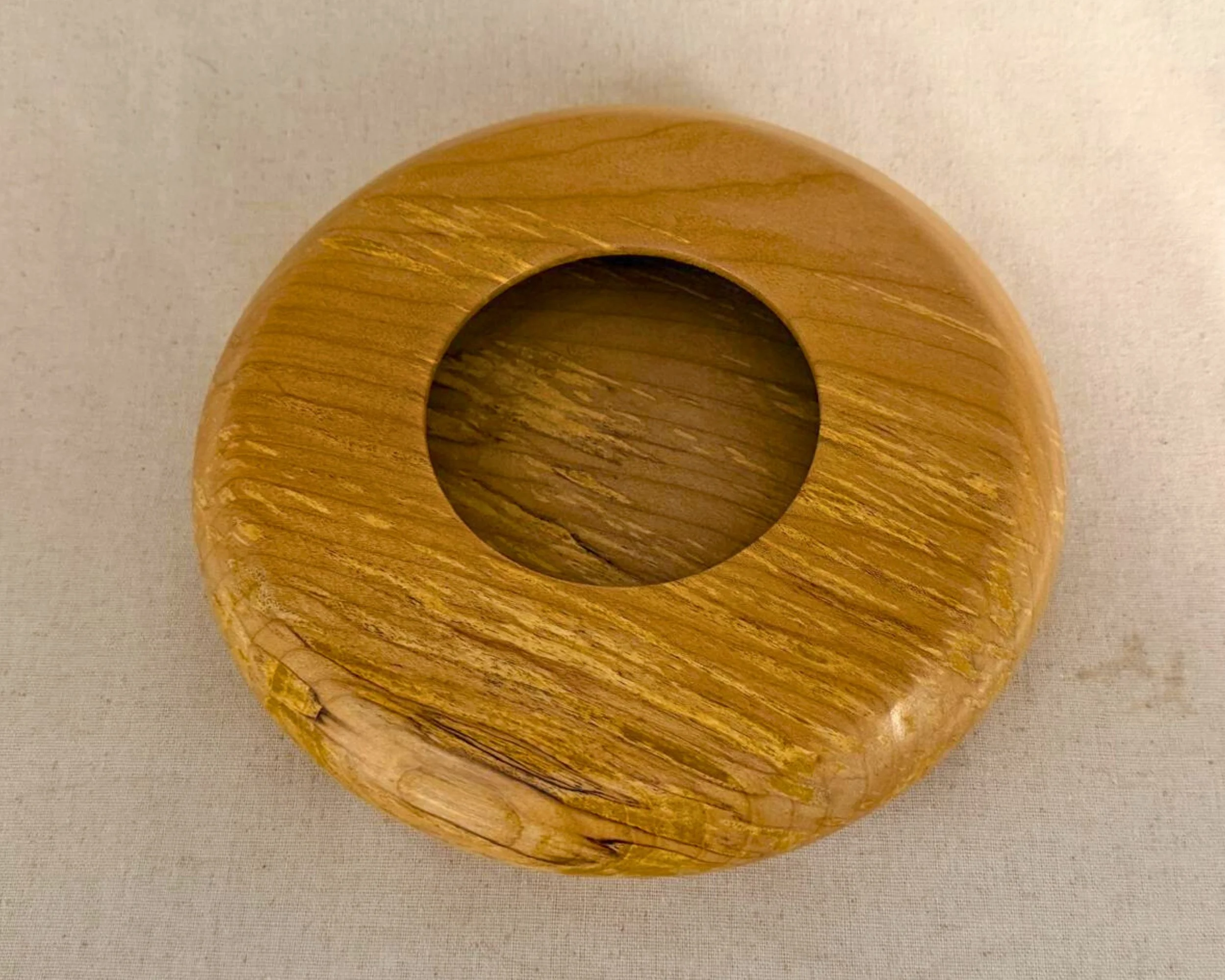 Top-down view of a hand-turned figured maple closed form vessel with a centered circular opening and flowing grain.
