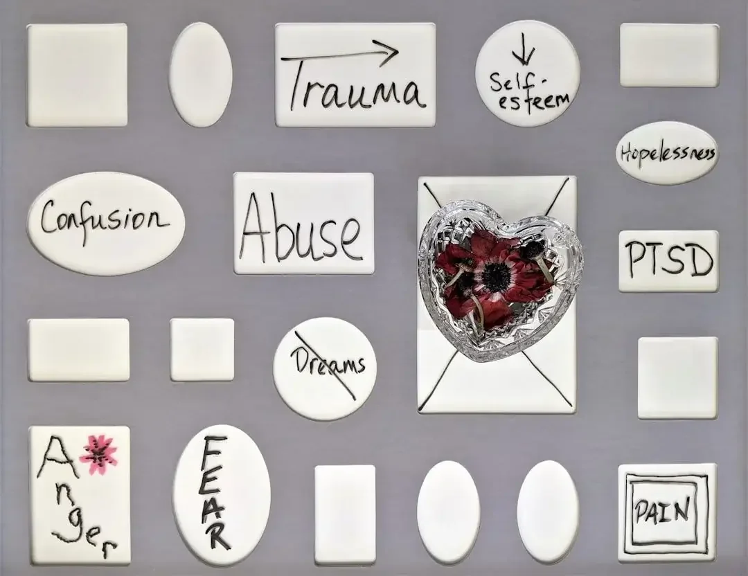 A bulletin board with notes about trauma, self-esteem, hope, confusion, abuse, PTSD, dreams, anger, fear, and pain. There is a heart-shaped container filled with dried flowers and pins in the center.